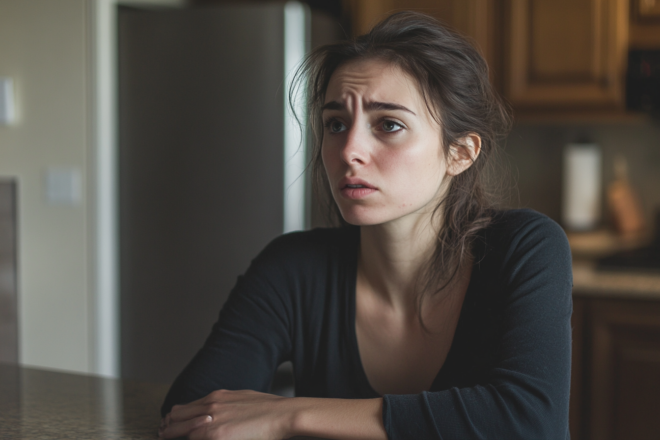 Une femme triste et choquée assise à la table de la cuisine | Source : Midjourney