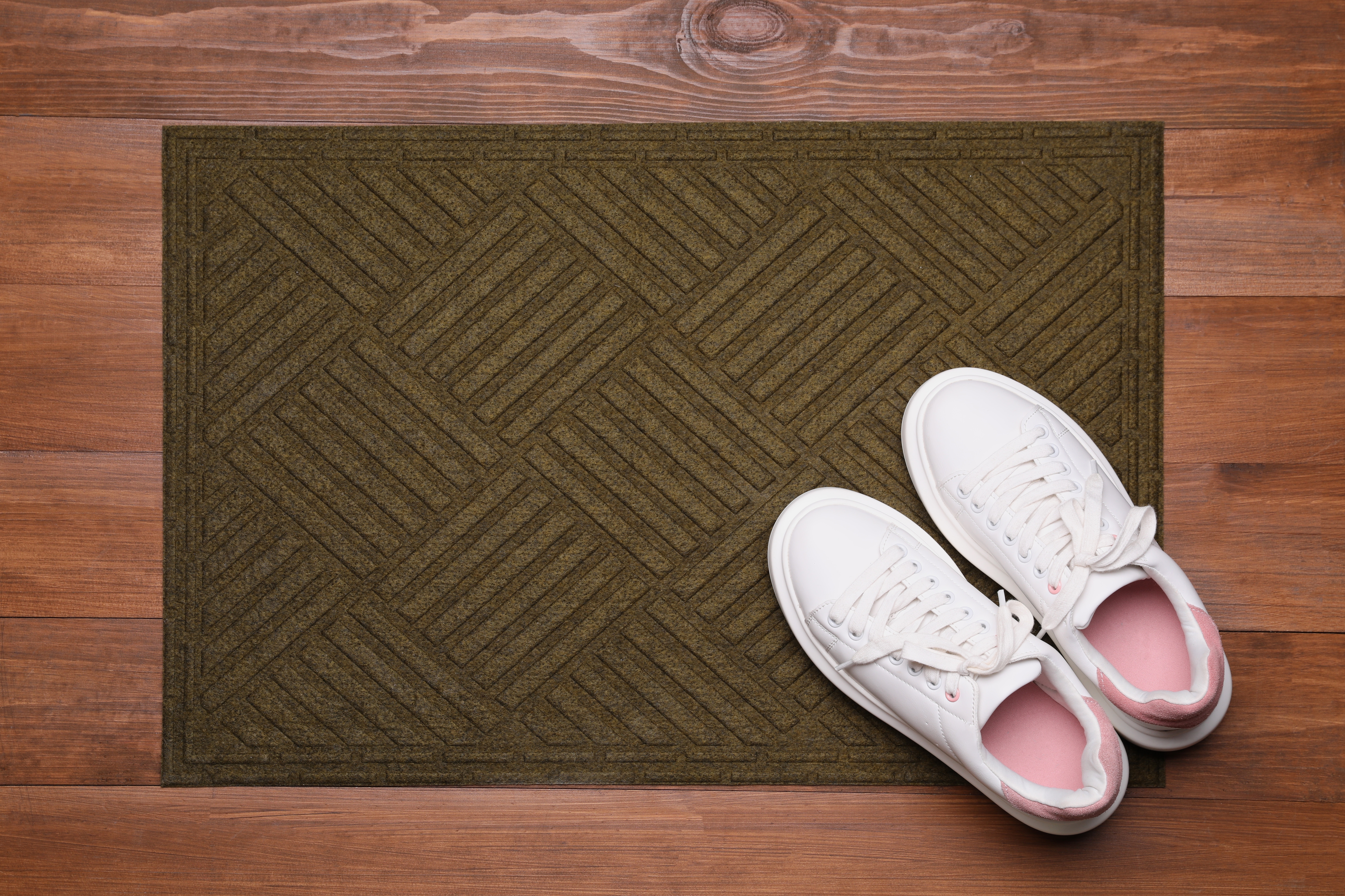 Une paire de baskets blanches est placée sur un paillasson posé sur le sol en bois | Source : Shutterstock