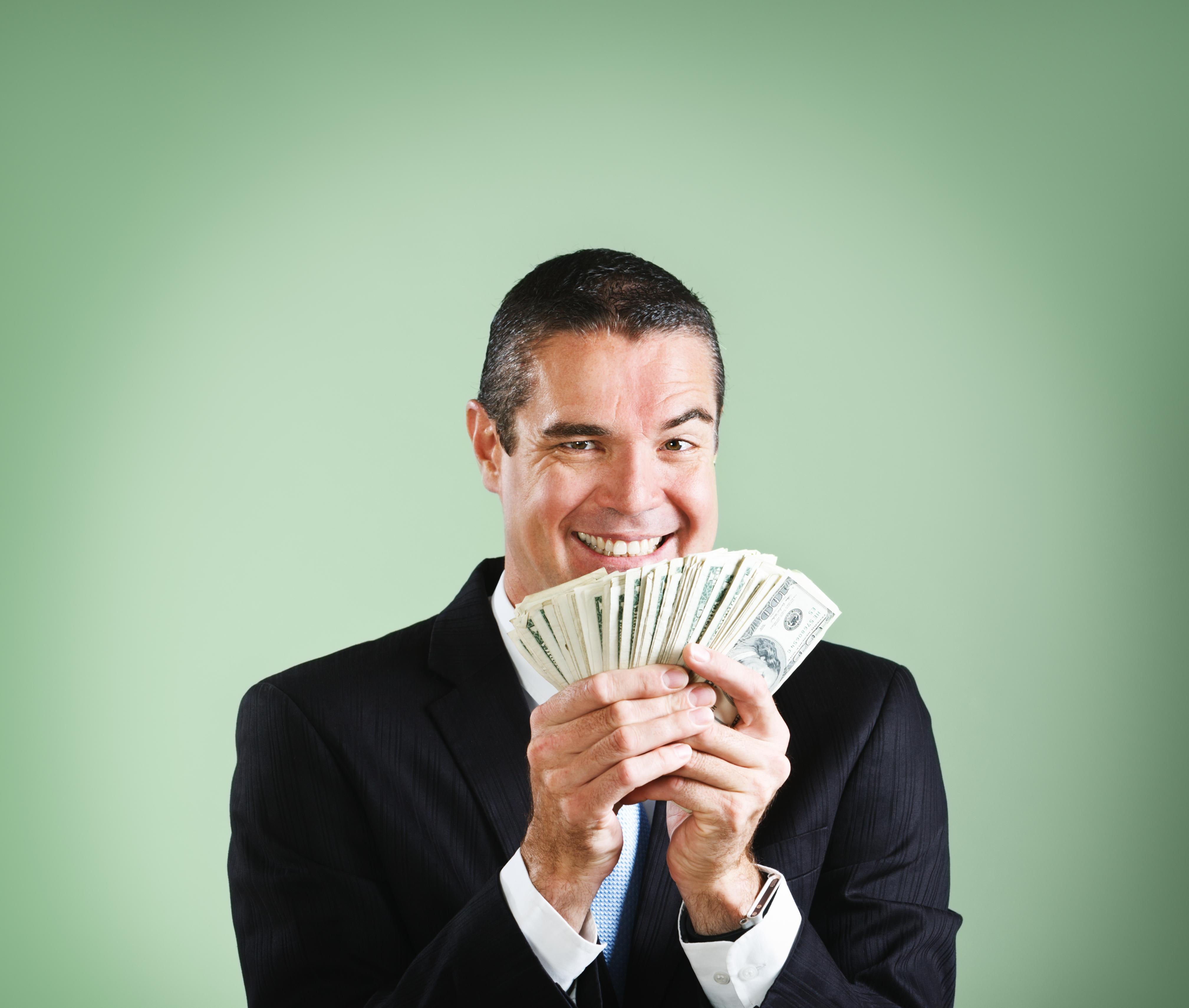 Un homme d'affaires sourit, jubilant devant une poignée de dollars | Source : Getty Images