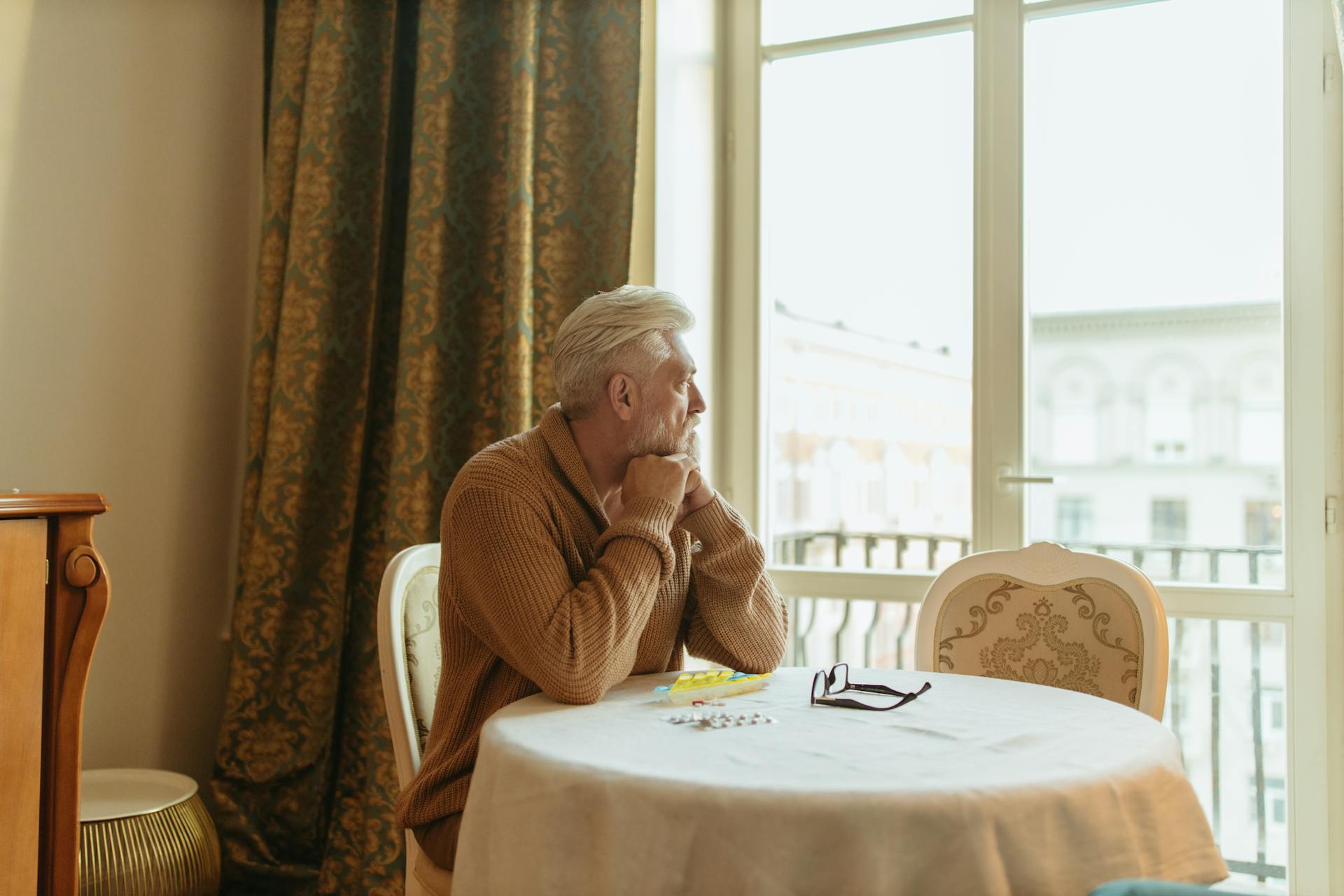 Un homme âgé assis sur une chaise avec des médicaments posés devant lui sur la table | Source : Pexels