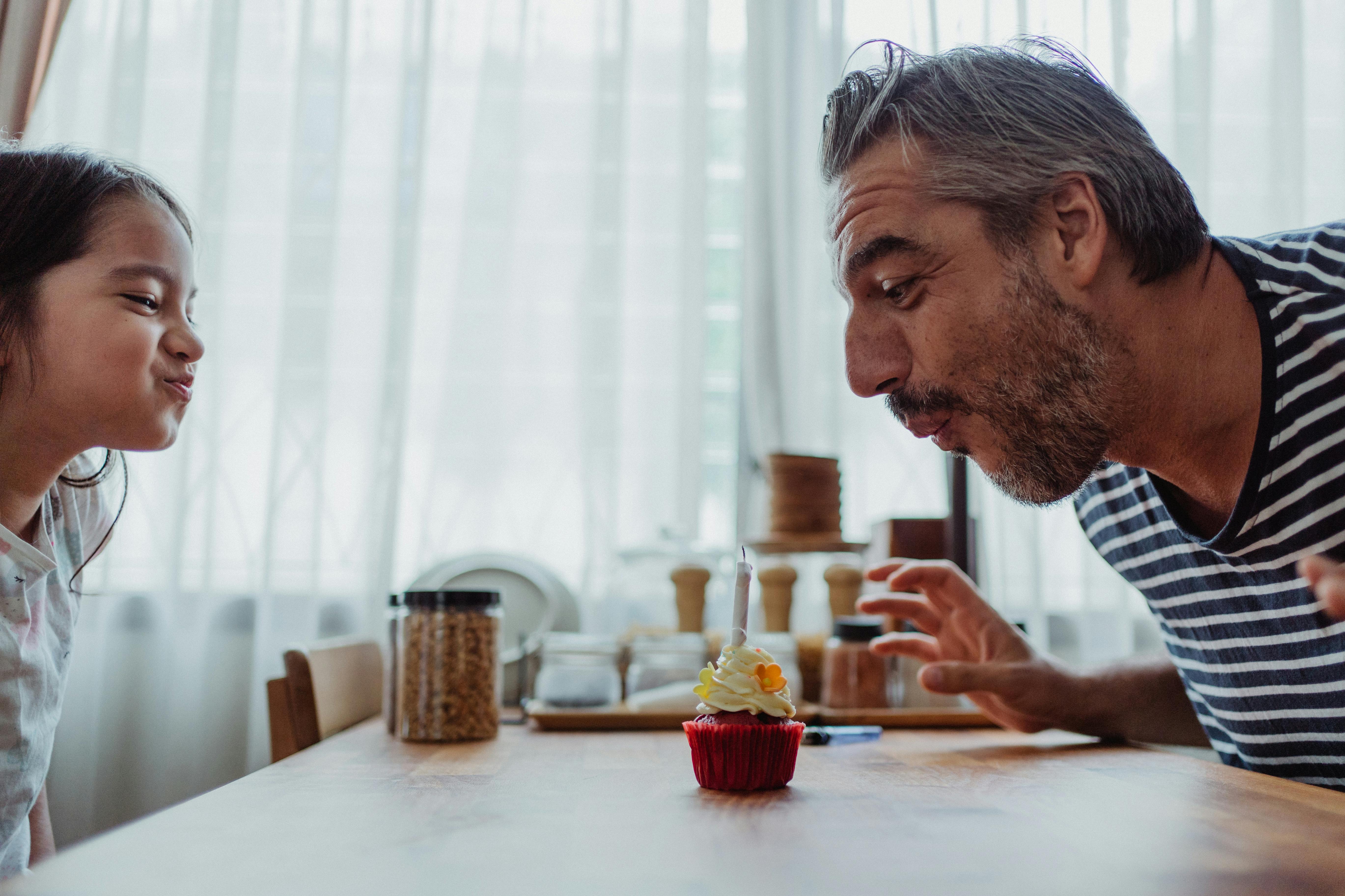 Un homme et une petite fille soufflant sur une bougie sur un cupcake | Source : Pexels