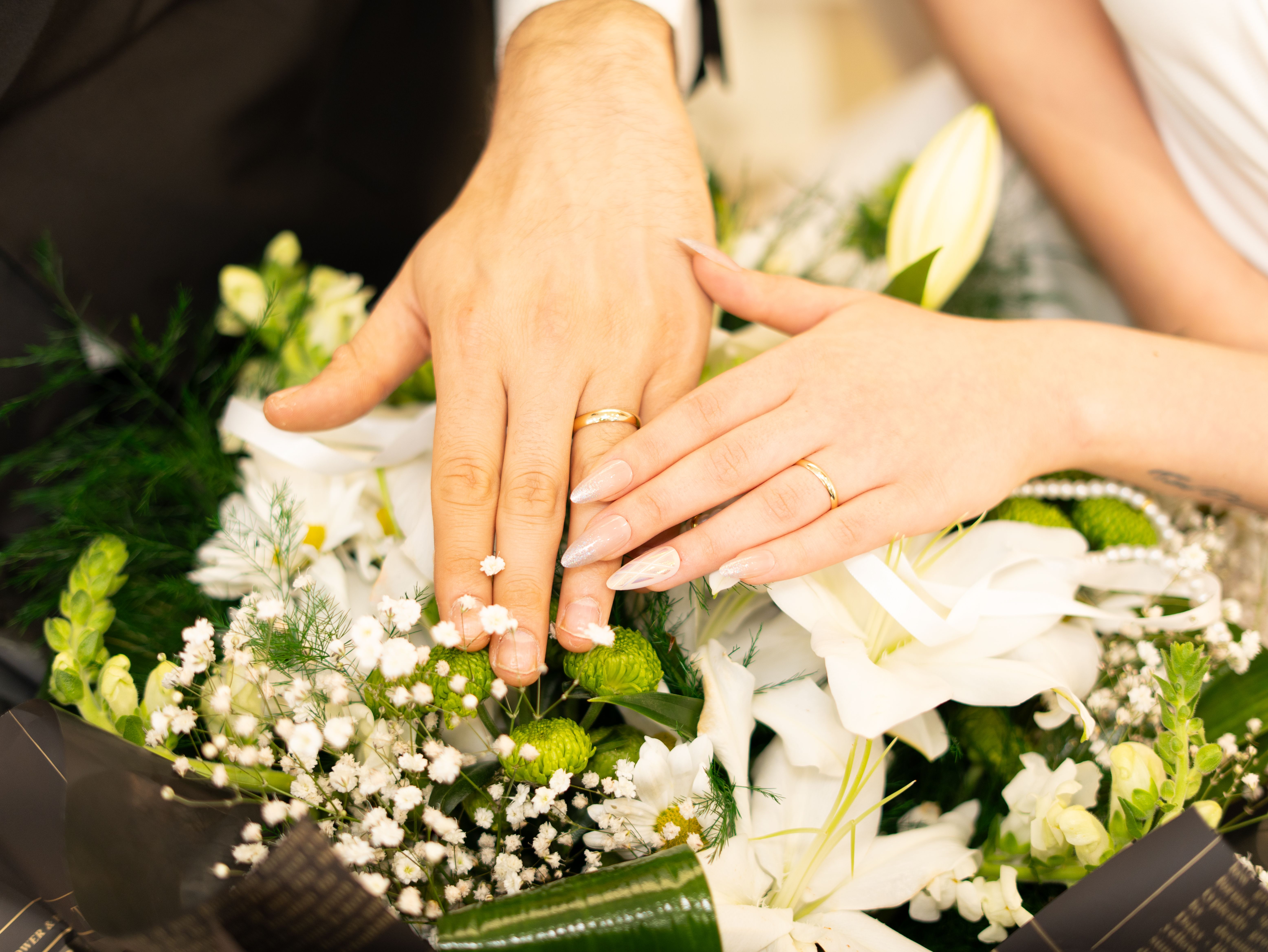 Gros plan sur des mains portant des alliances, posées sur un bouquet de fleurs | Source : Pexels