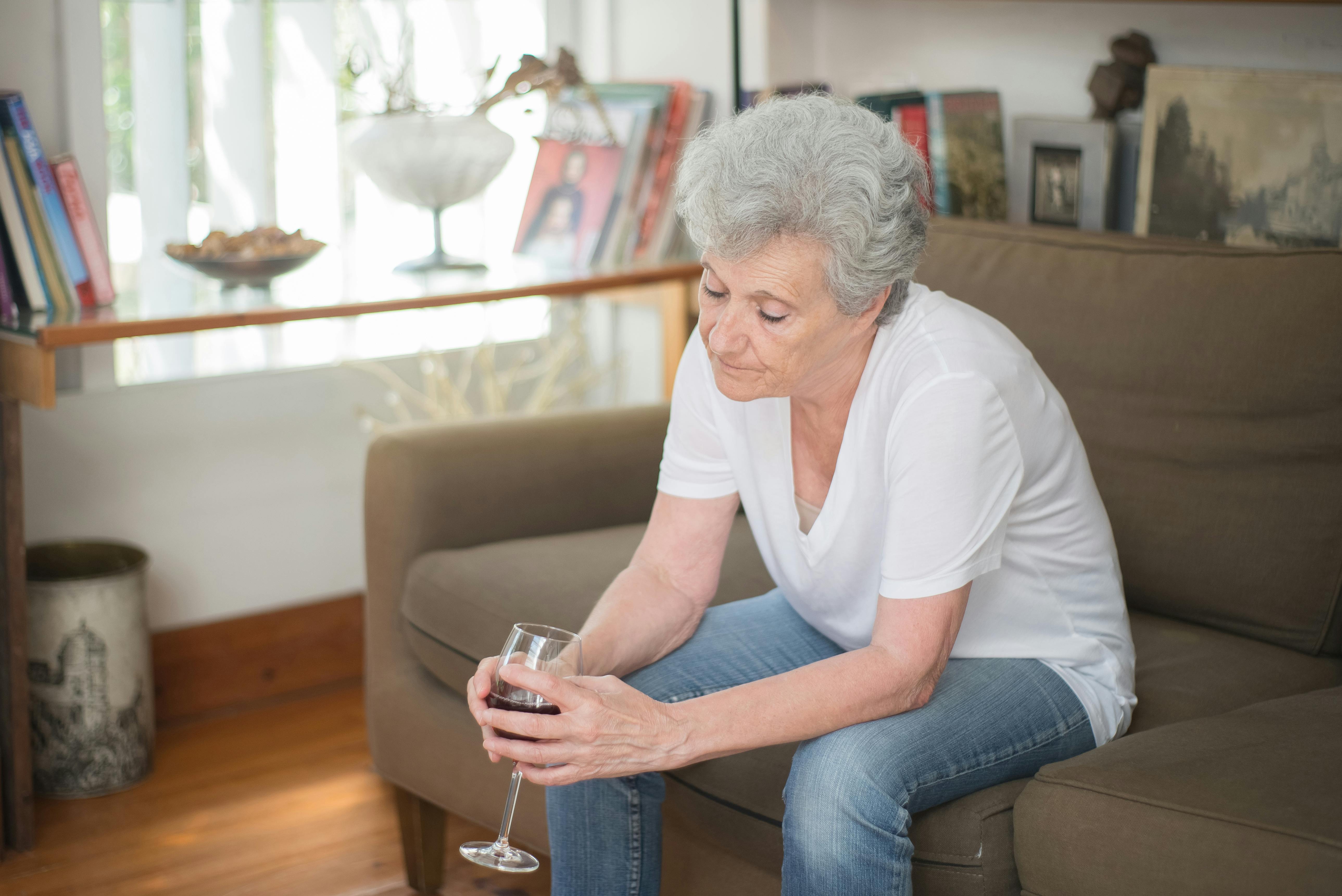 Une femme âgée contrariée tenant un verre de vin alors qu'elle est assise sur un canapé | Source : Pexels