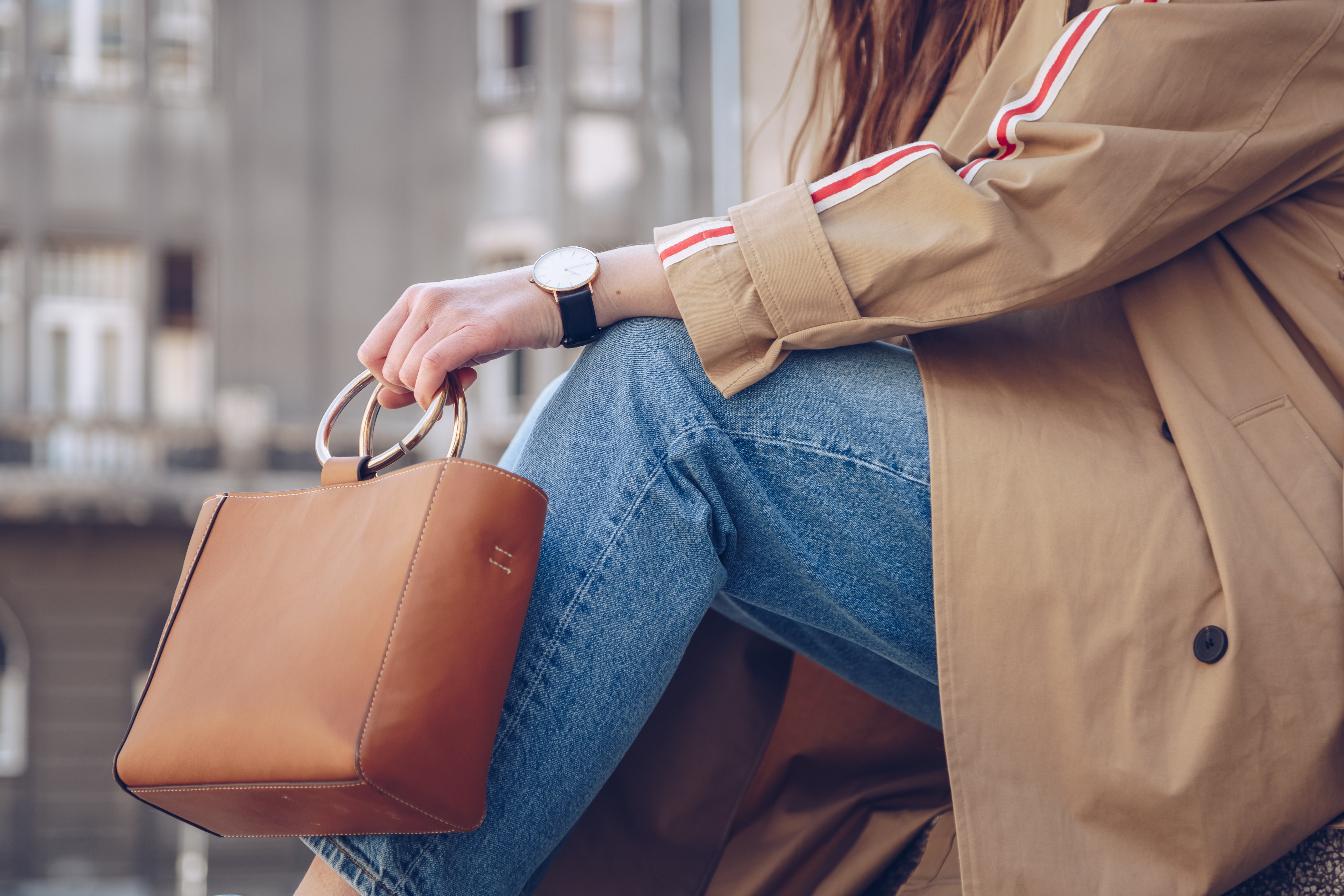 détails du style de rue. femme séduisante portant un manteau de tranchée beige, jeans denim, bottes de cheville, montre et sac en cuir à poignée métallique. tenue de mode parfaite pour un printemps ensoleillé | Photo : Shutterstock