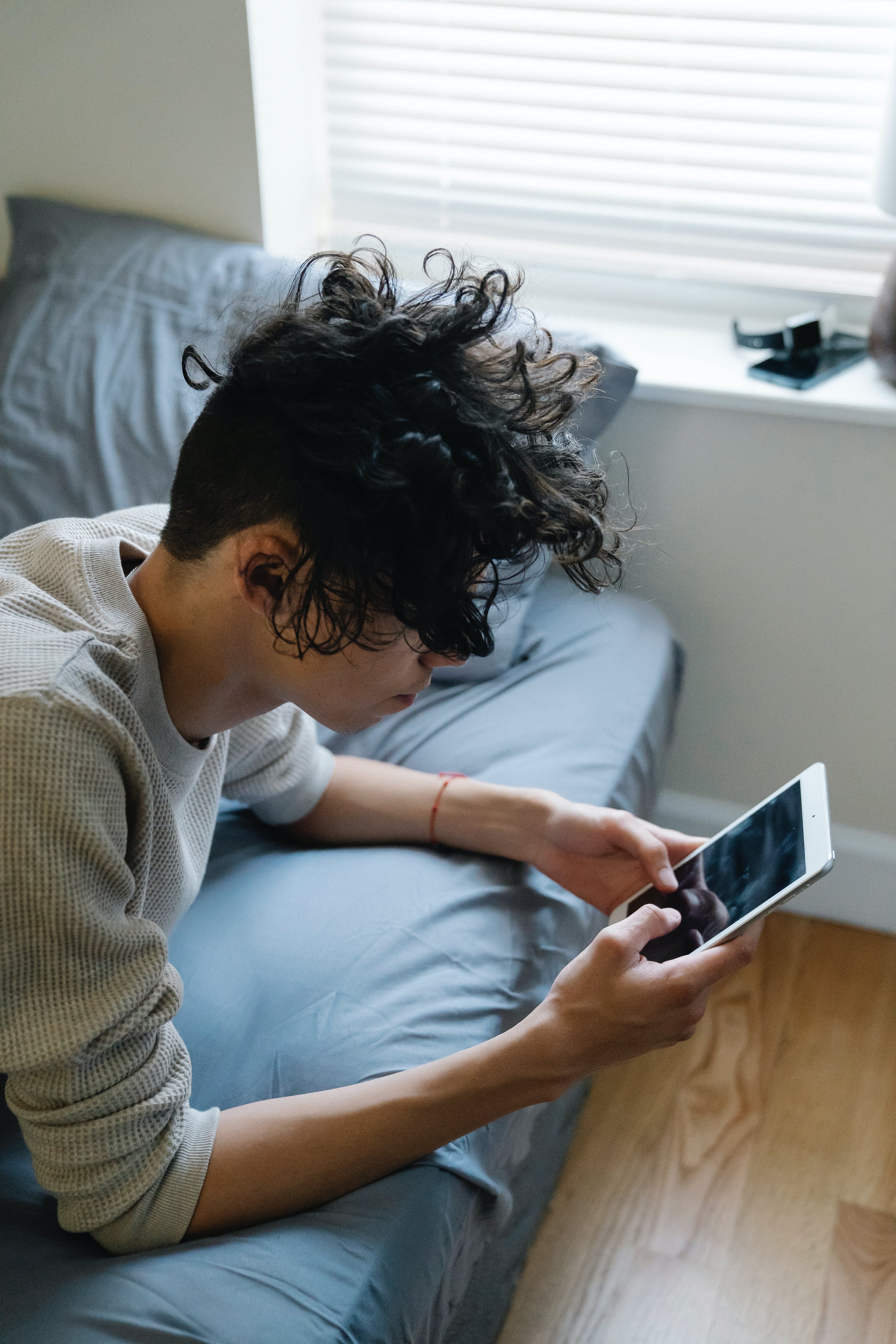 Un jeune homme envoyant des textos sur un téléphone alors qu'il est allongé sur un lit | Source : Pexels