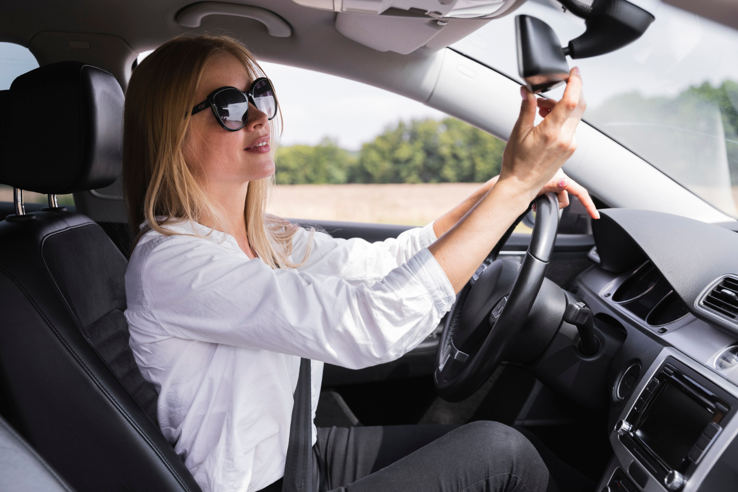 Une femme conduit sa voiture tout en ajustant le rétroviseur | Source : Freepik