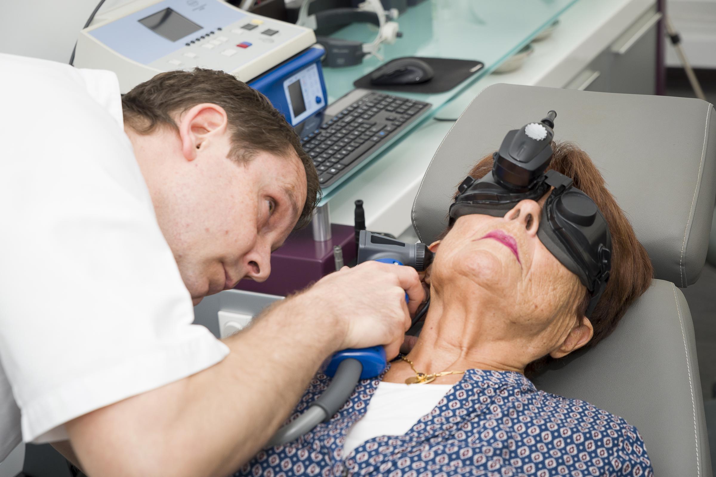 Un médecin effectue un examen de l'oreille pendant qu'une patiente subit un test d'équilibre avec des lunettes de diagnostic à infrarouge | Source : Getty Images