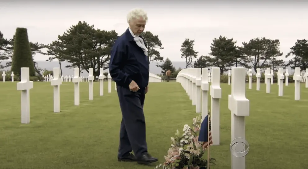 Peggy Harris se tient à côté de la tombe de son défunt mari, Billie Harris, ornée de fleurs. | Source : YouTube.com/CBS News