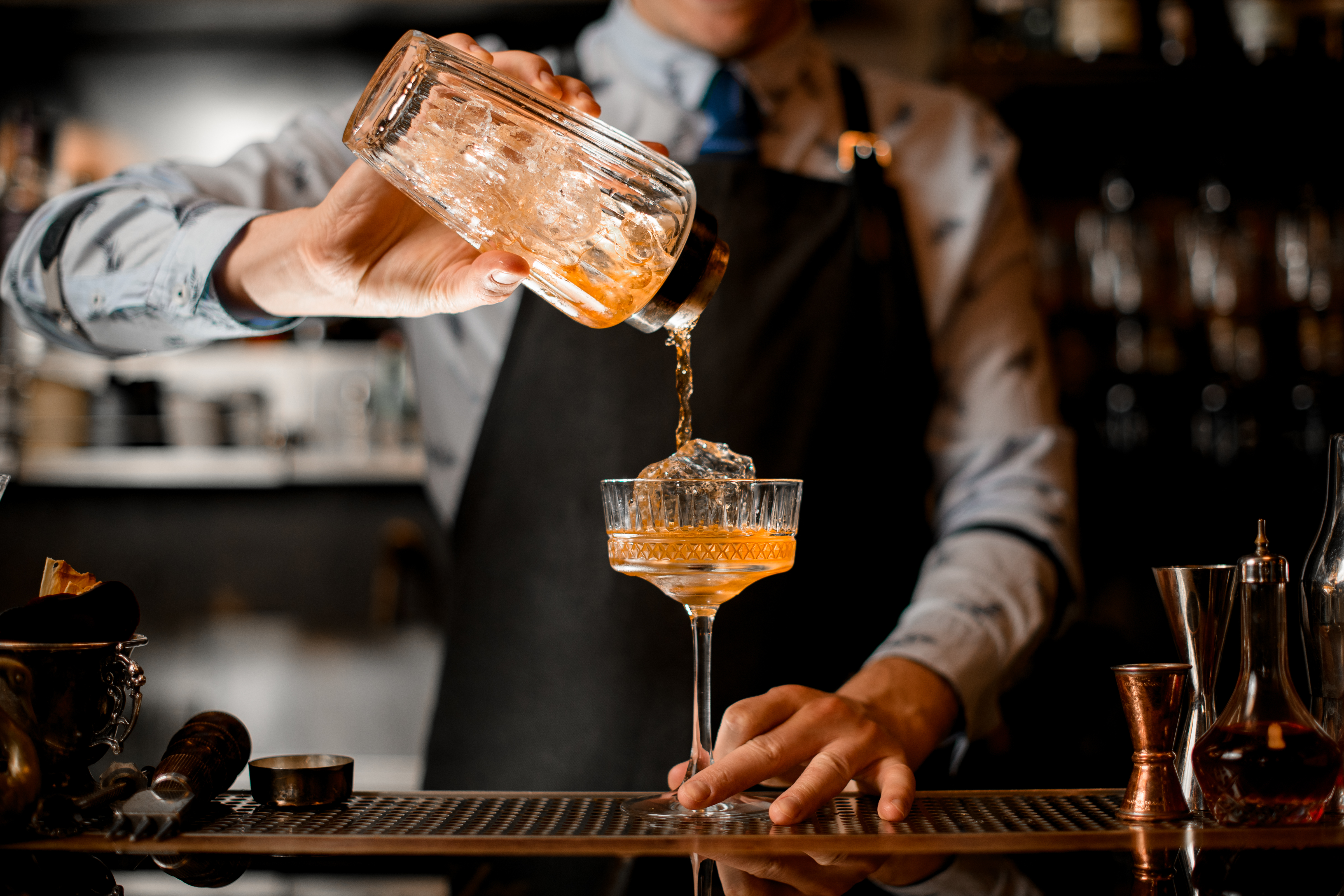 O barman derrama suavemente o coquetel acabado da coqueteleira em vidro. | Fonte: Shutterstock