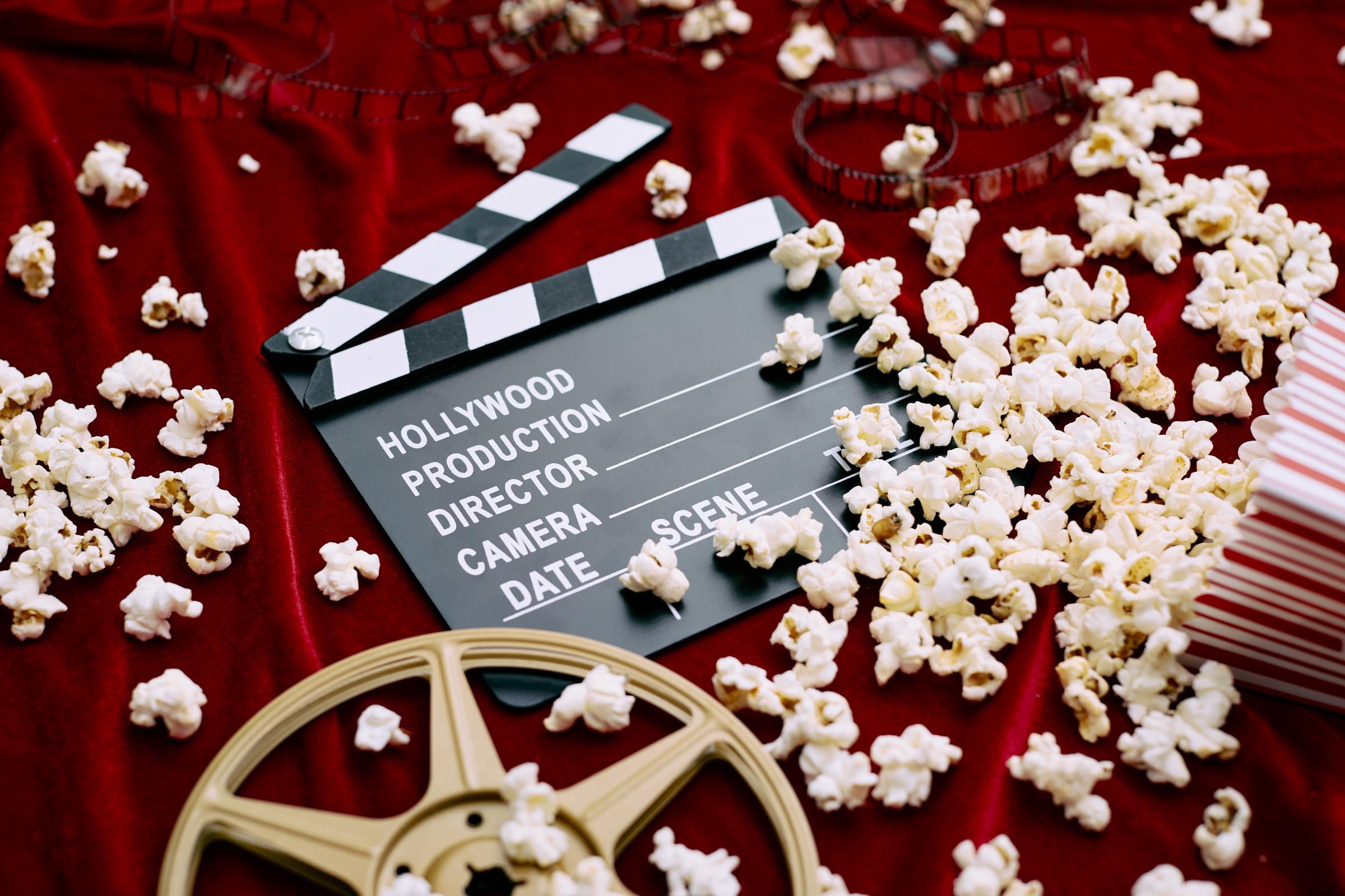 Un clap, une bobine de film, un film et du pop-corn renversé sur un fond de satin rouge | Source : Getty Images