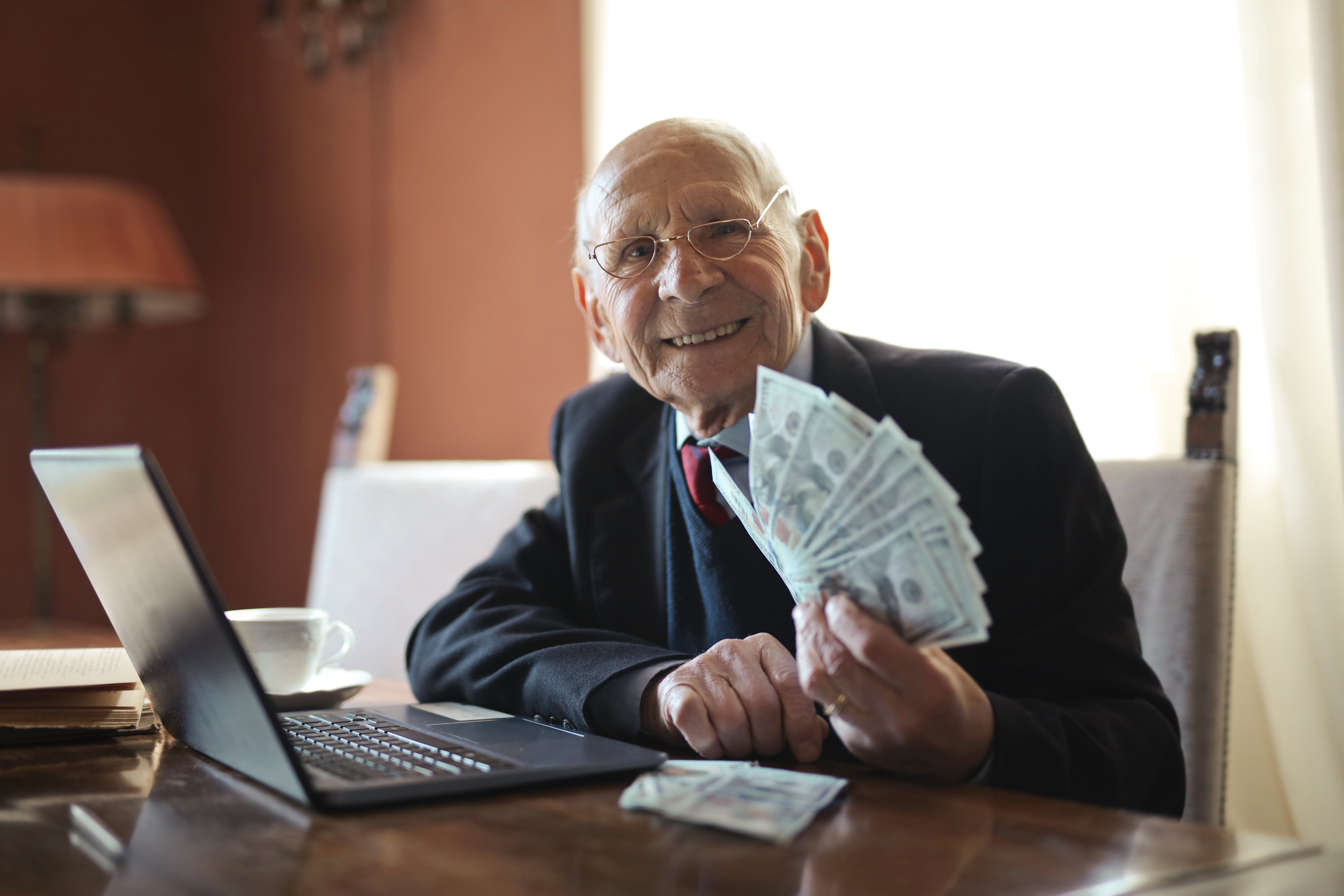 Un anciano sonríe mientras sostiene dinero. | Fuente: Pexels