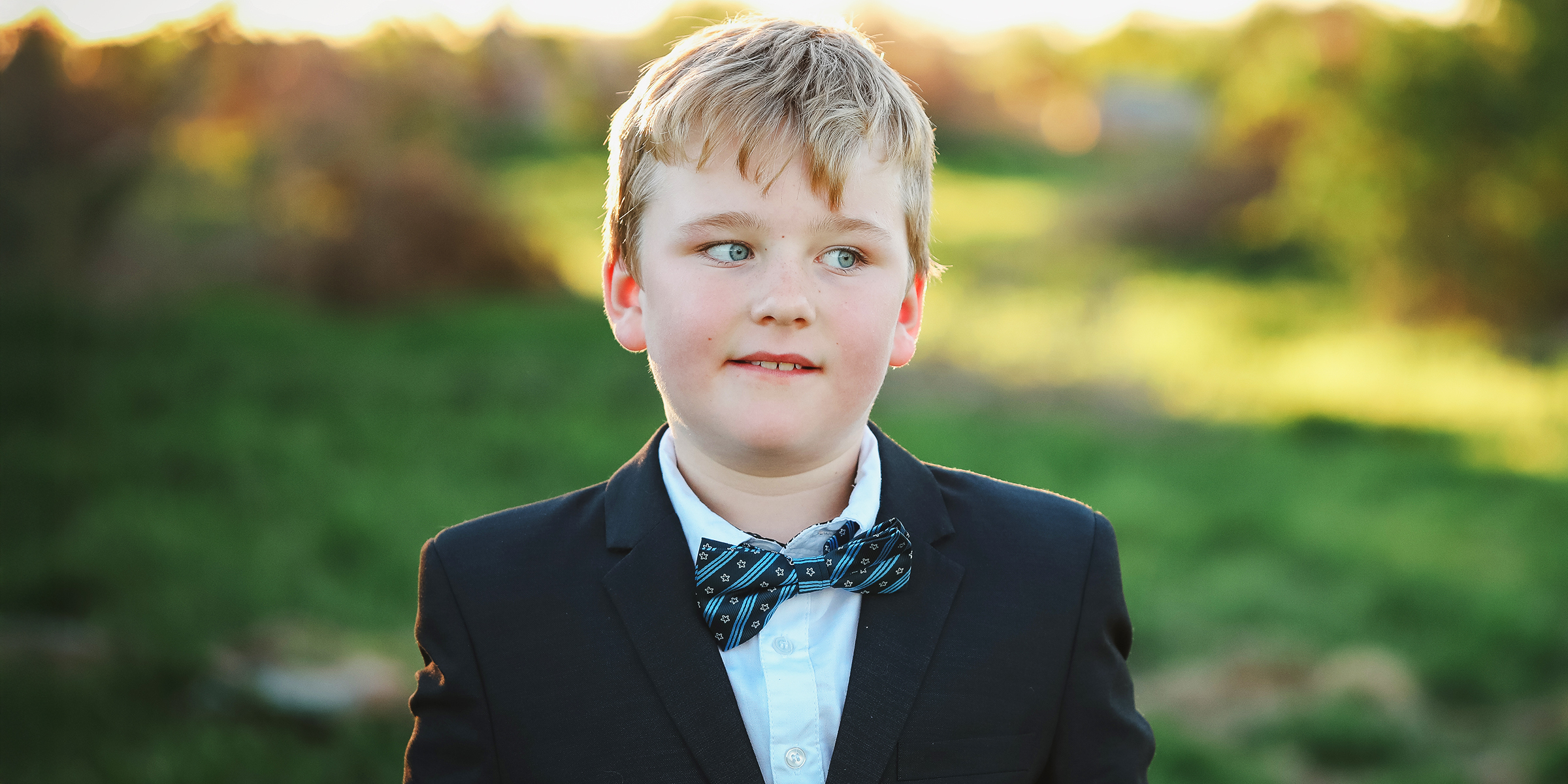 Un jeune garçon en costume et nœud papillon debout à l'extérieur | Source : Shutterstock