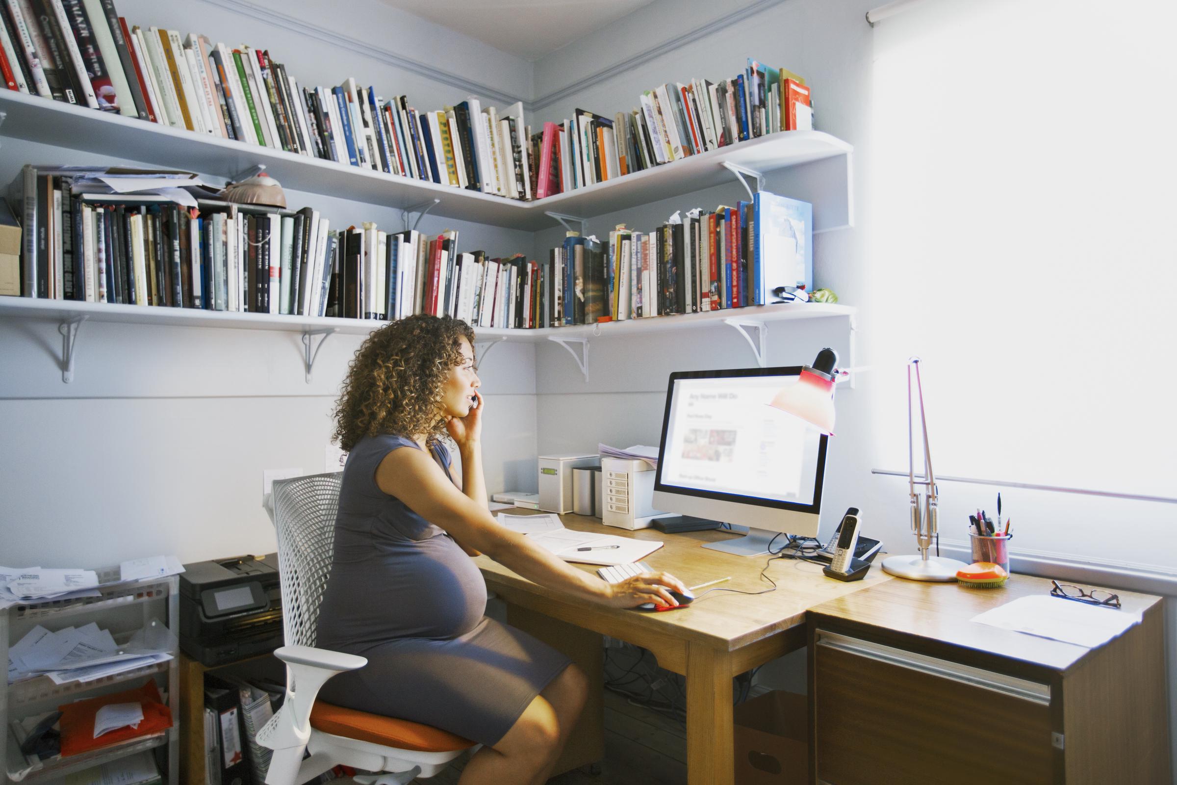 Une femme enceinte travaille depuis chez elle, assise à son bureau devant son ordinateur I Photo d'illustration I Source : Getty Images