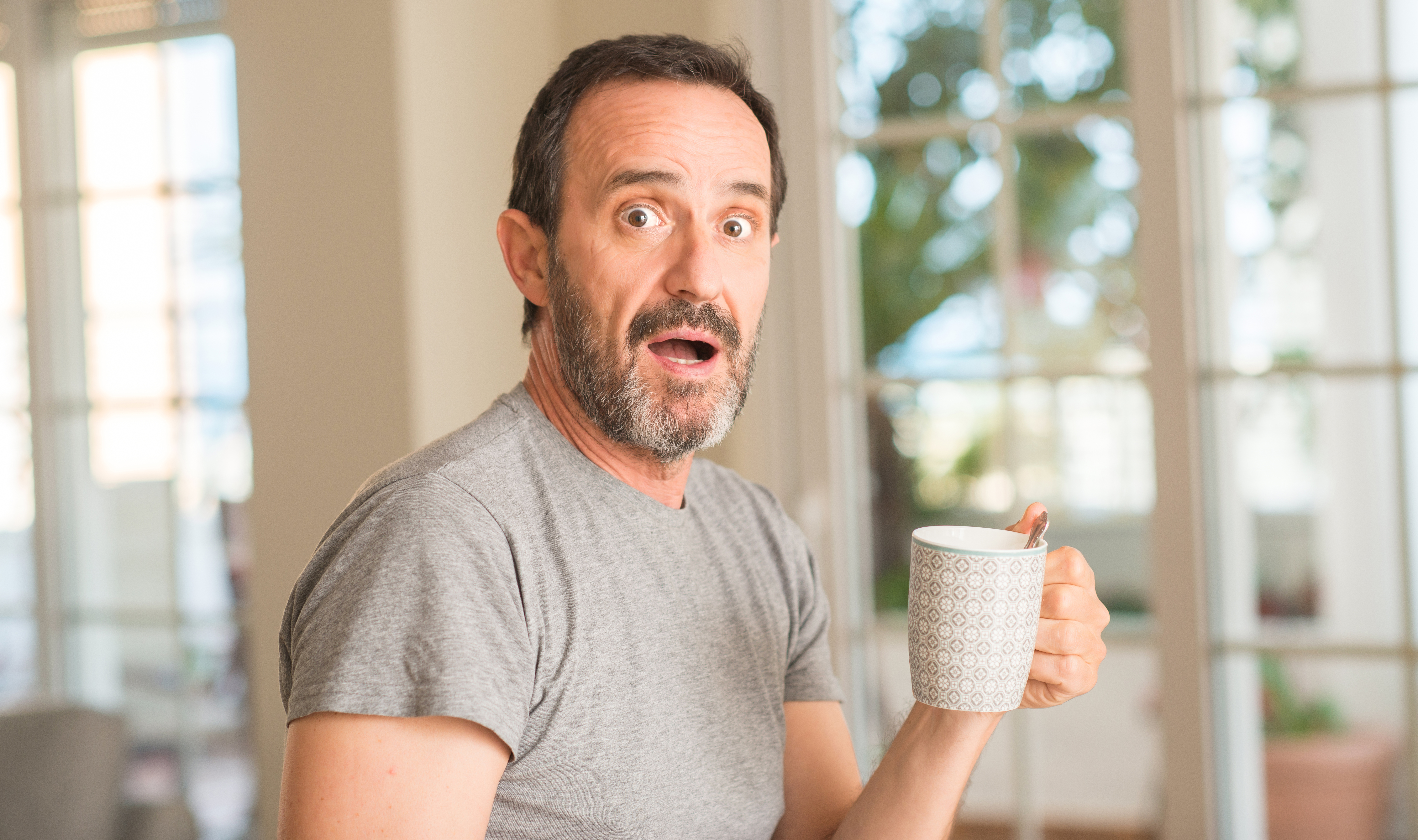 Homme d'âge moyen buvant du café dans une tasse en état de choc | Source : Getty Images