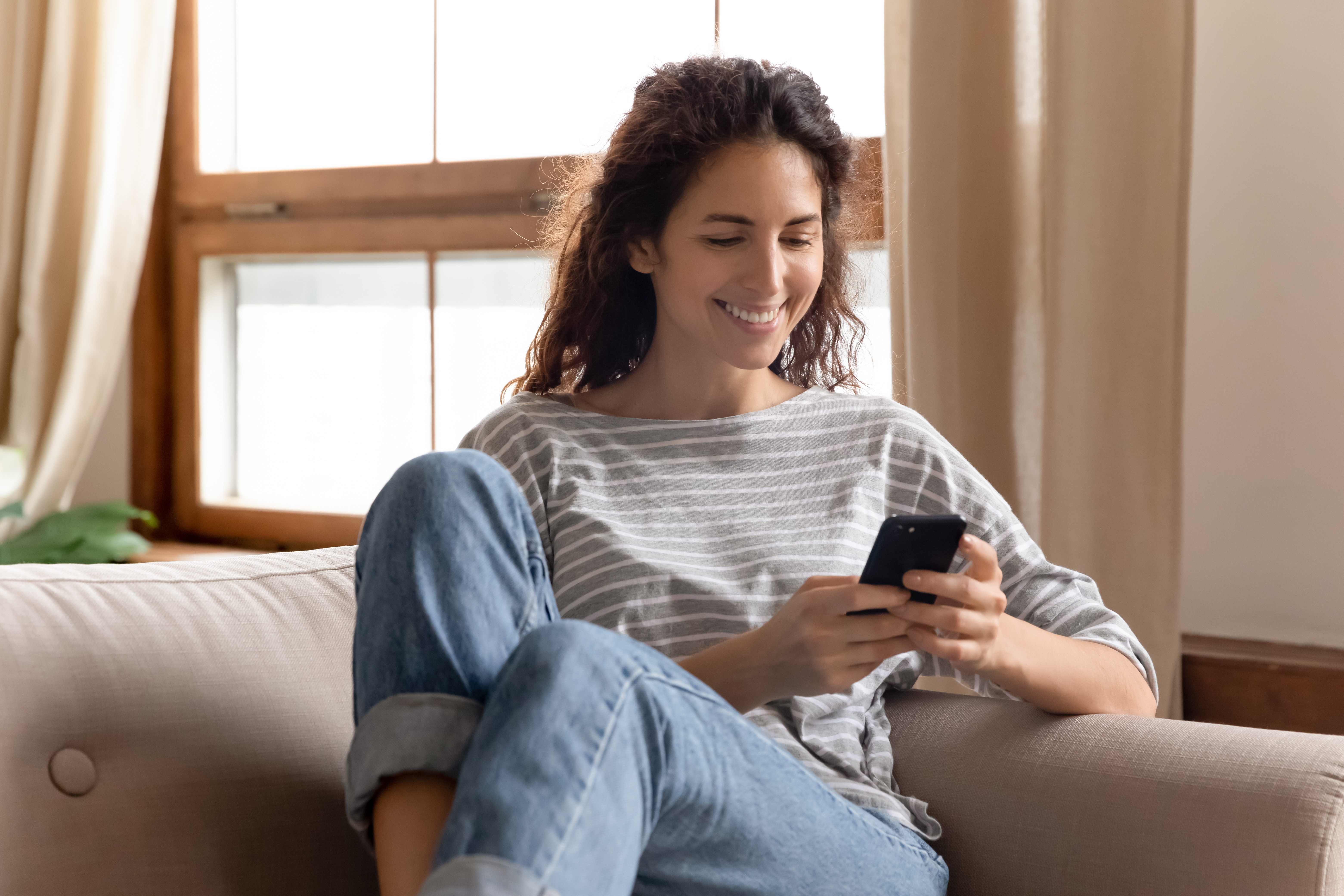 Une femme souriant en regardant son téléphone portable | Source : Shutterstock