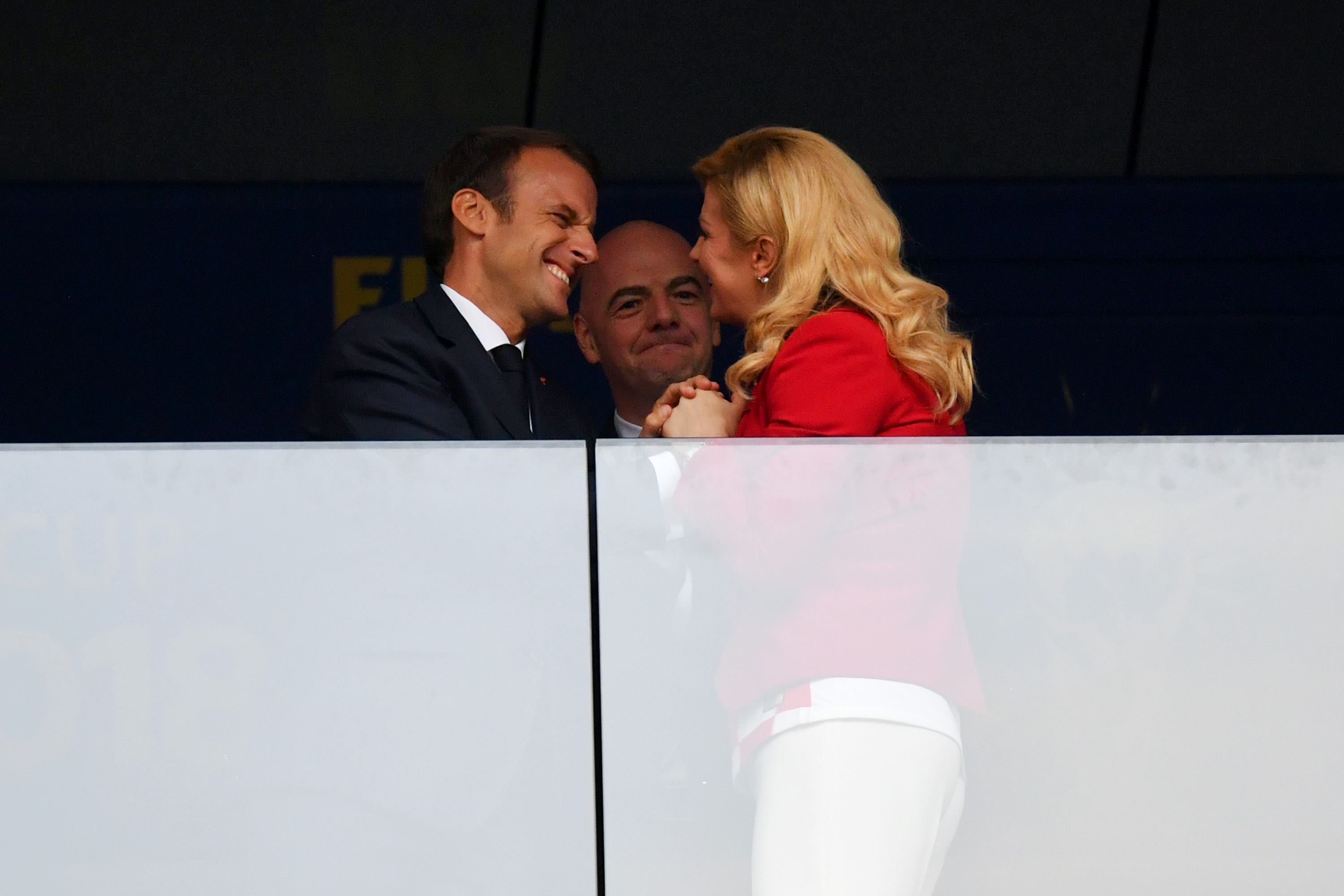 Emmanuel Macron et Kolinda Grabar-Kitarović partagent un moment de gaieté en se penchant tout près, en souriant et en maintenant le contact des mains pendant que Gianni Infantino regarde derrière eux.