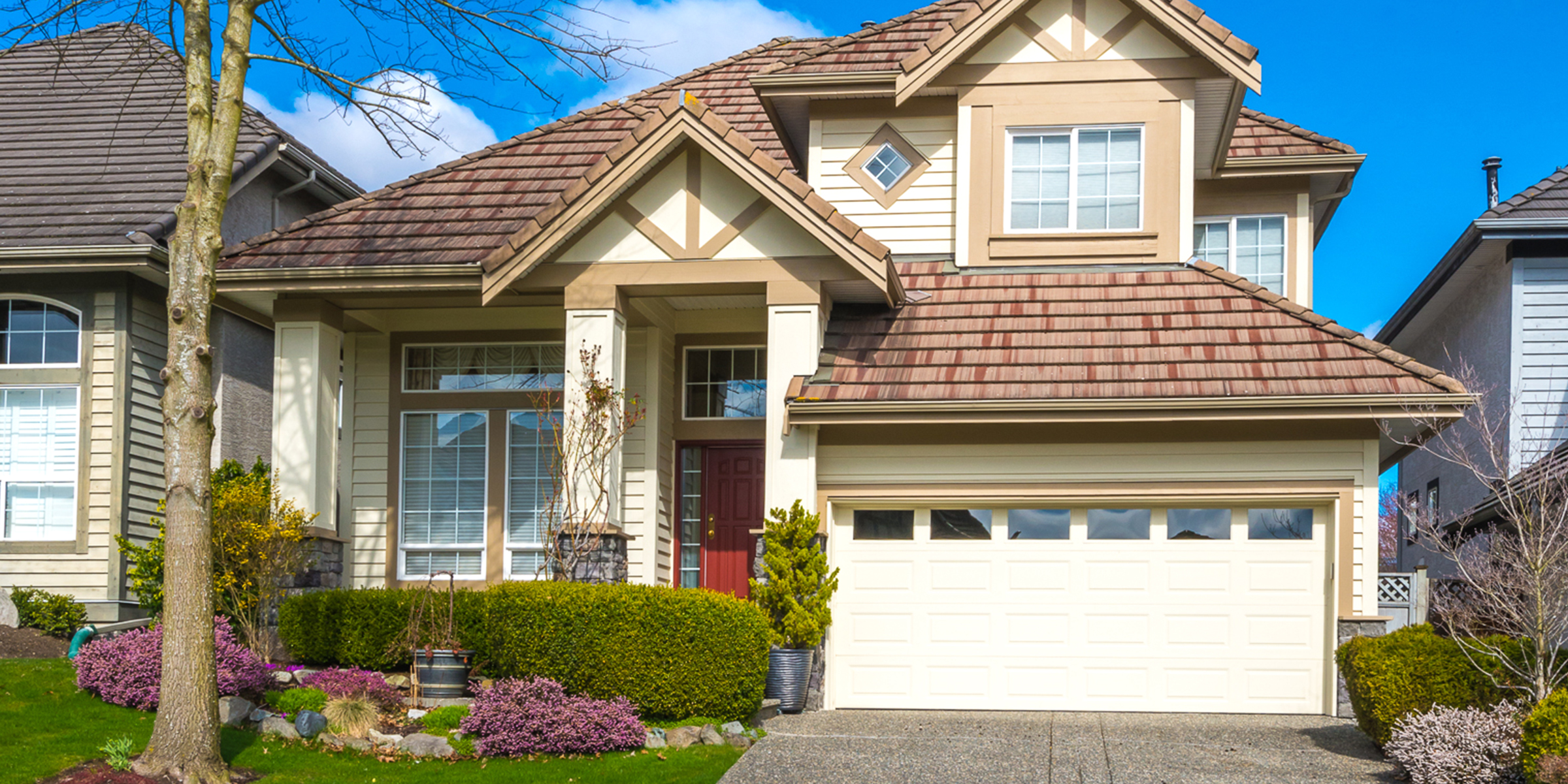 Une maison de banlieue avec une porte d'entrée rouge, un aménagement paysager manucuré et un extérieur lumineux et accueillant | Source : Shutterstock