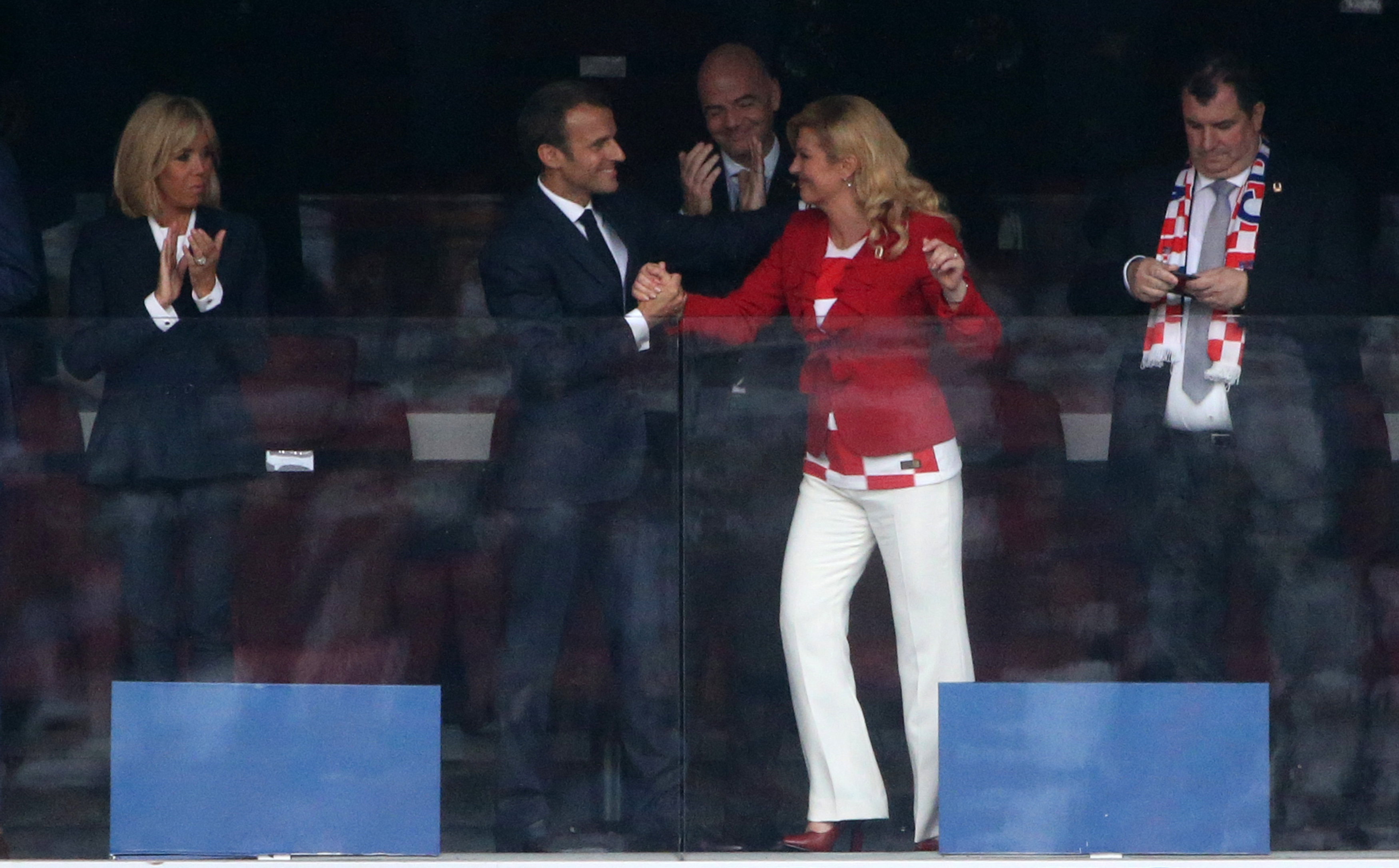 Emmanuel Macron et Kolinda Grabar-Kitarović continuent de se tenir la main et d'échanger des sourires, célébrant dans les tribunes alors que d'autres applaudissent autour d'eux.