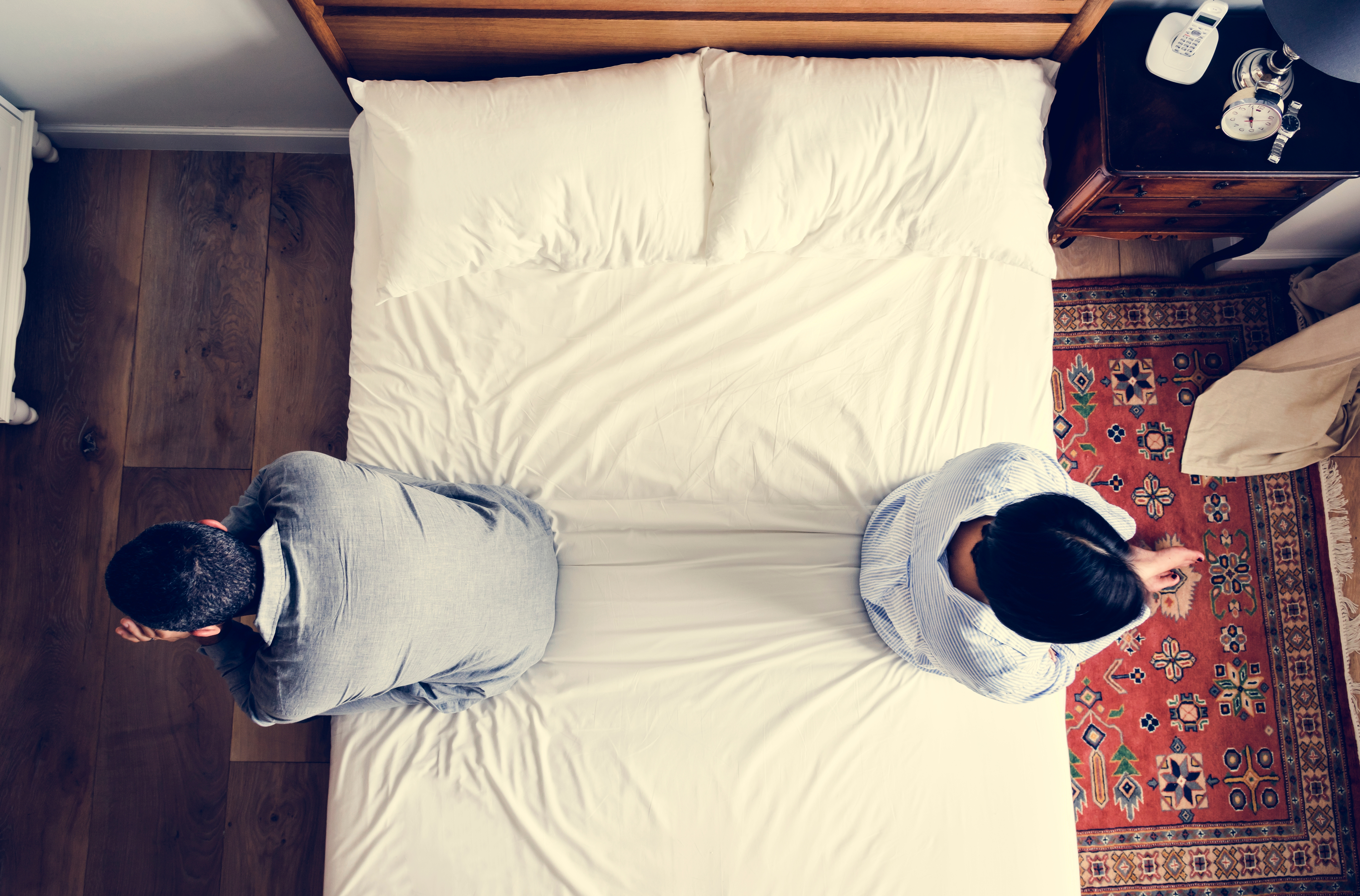 Un couple assis sur les extrémités opposées de leur lit après une dispute | Source : Shutterstock
