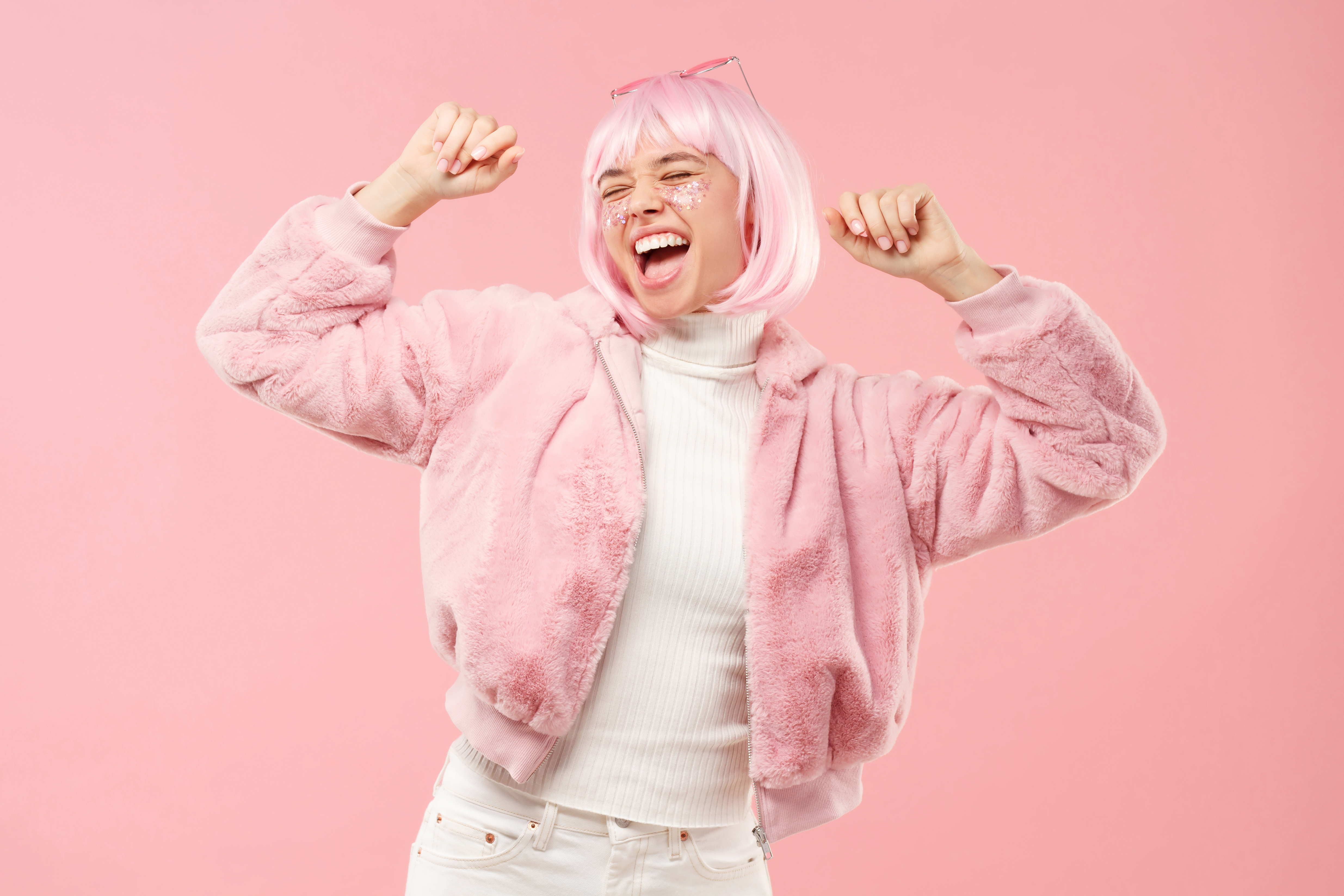 Adolescente excitée qui danse au son de la musique, portant un manteau de fourrure duveteux et des cheveux teints lors d'une fête, sur fond rose | Source : Getty Images