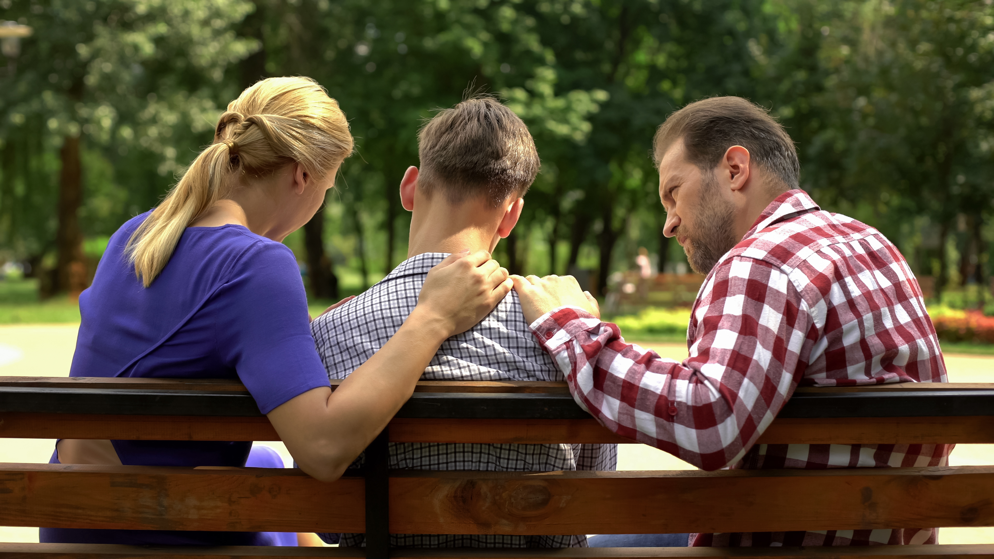Des parents parlent à leur fils adolescent dans un parc | Source : Shutterstock