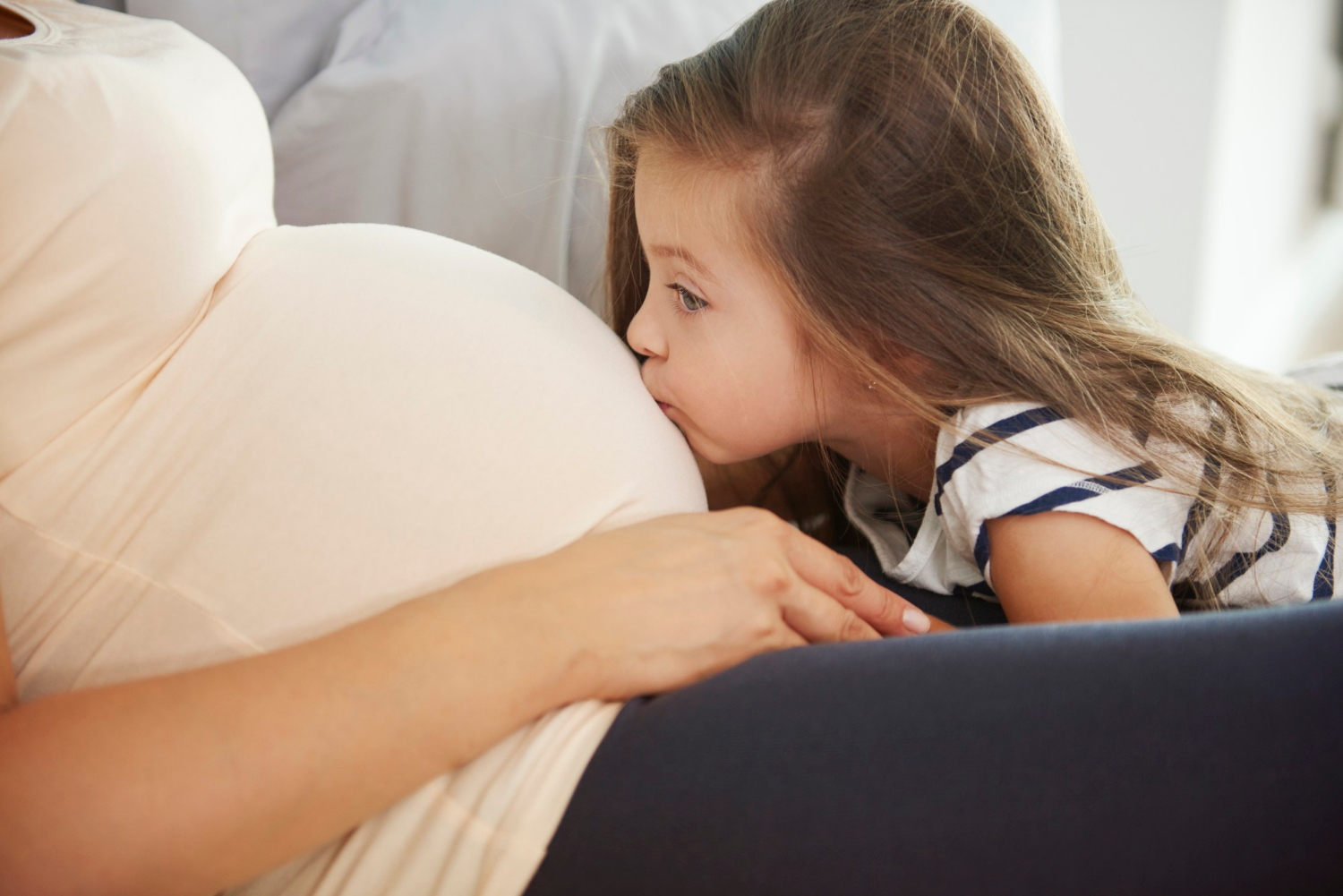 Une petite fille embrasse délicatement le baby bump de sa mère | Source : Freepik