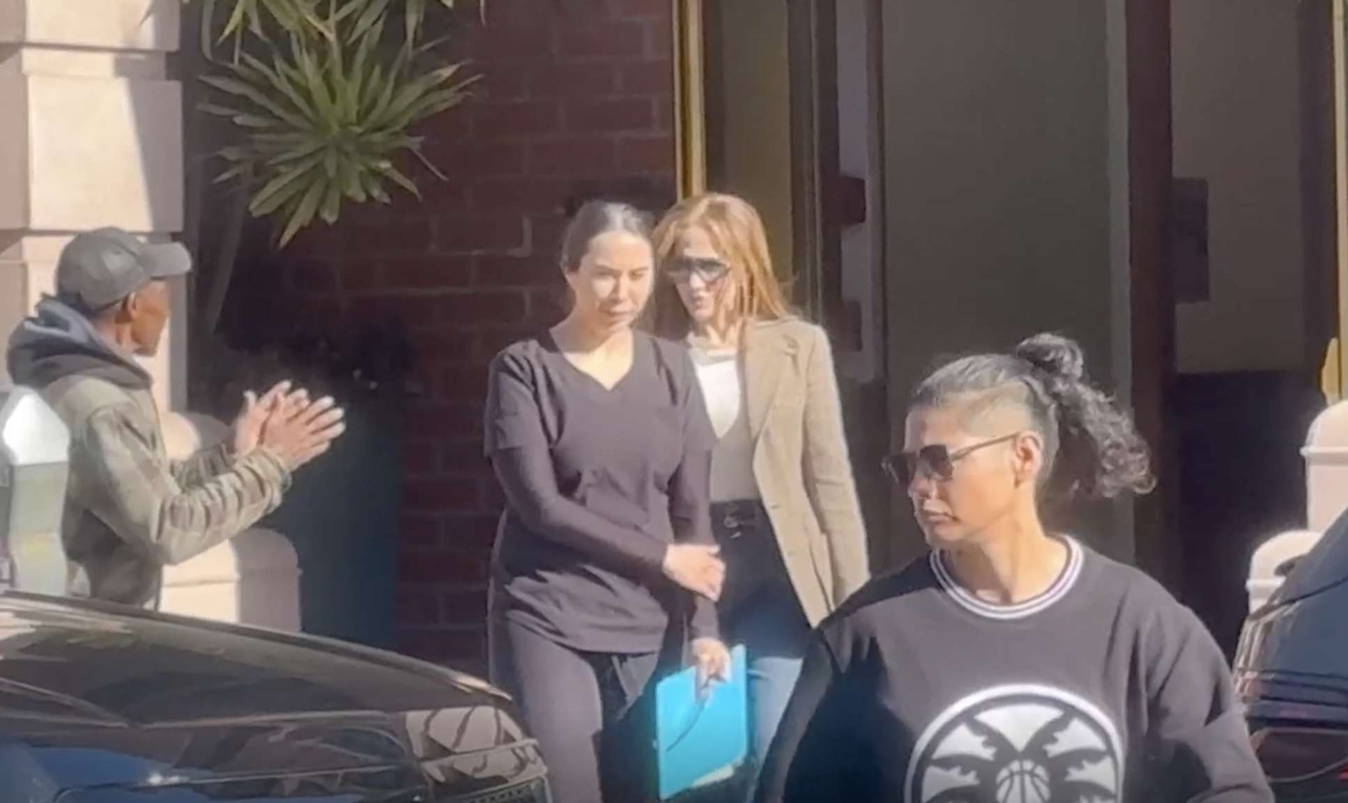Jennifer Lopez quitte le bâtiment avec d'autres personnes tandis qu'un sans-abri joint les mains à proximité | Source : YouTube/TMZ