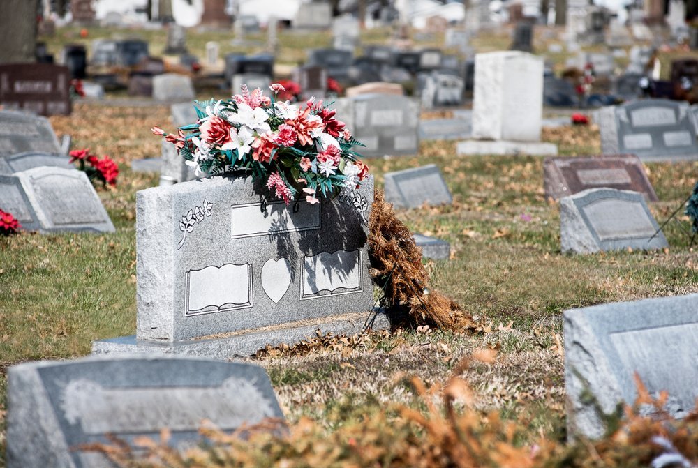 Pierre tombale dans un cimetière avec des fleurs et plus de pierres tombales en arrière-plan. | Shutterstock