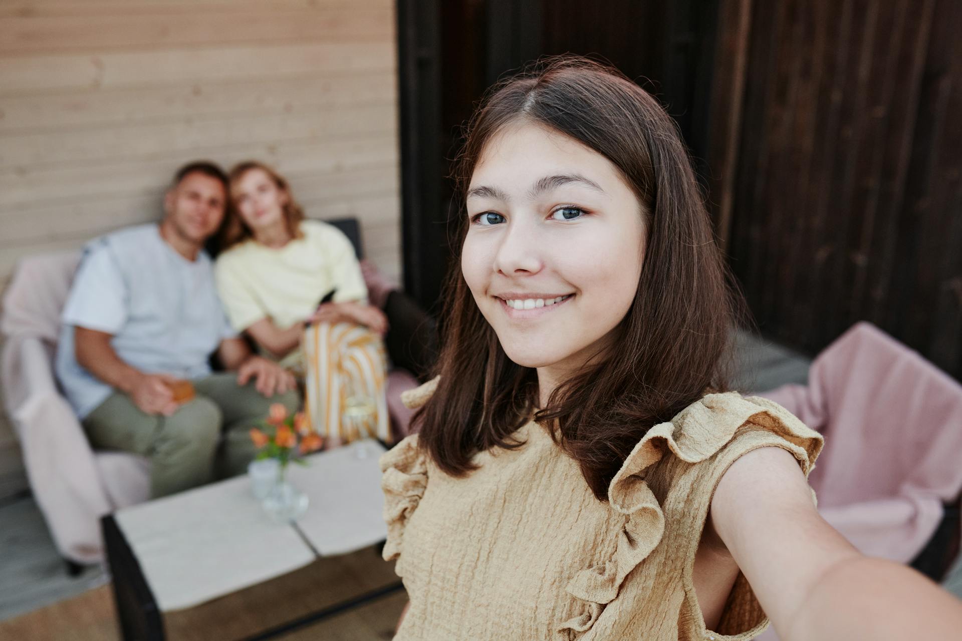 Une adolescente prenant un selfie avec deux adultes en arrière-plan | Source : Pexels