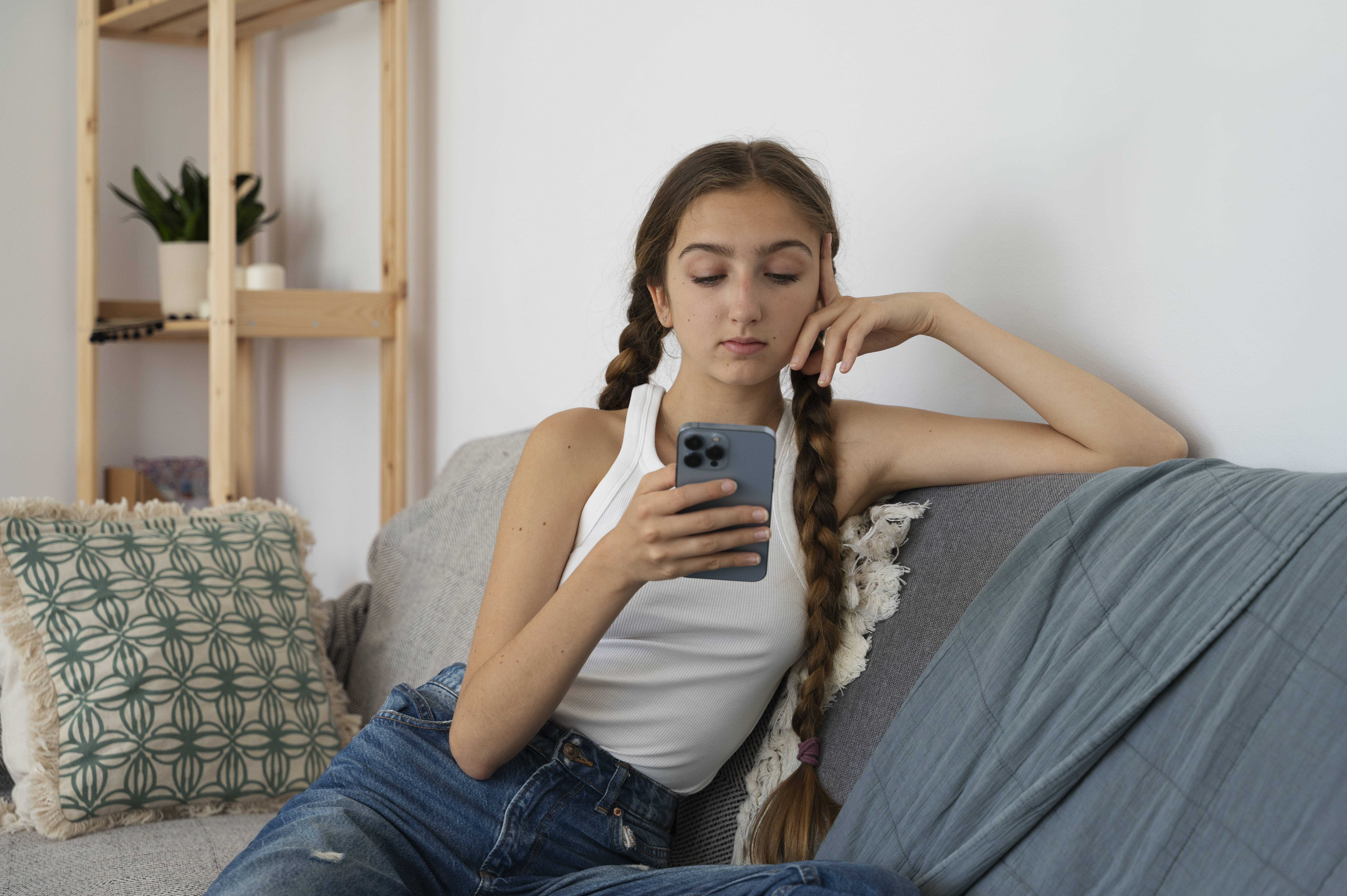 Jeune fille assise sur un canapé et fixant son téléphone portable | Source : Freepik