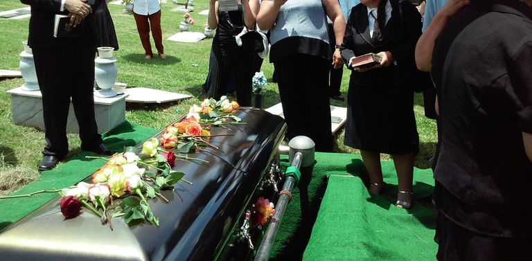 Des personnes rassemblées autour d'un cercueil orné de roses. | Source : Unsplash