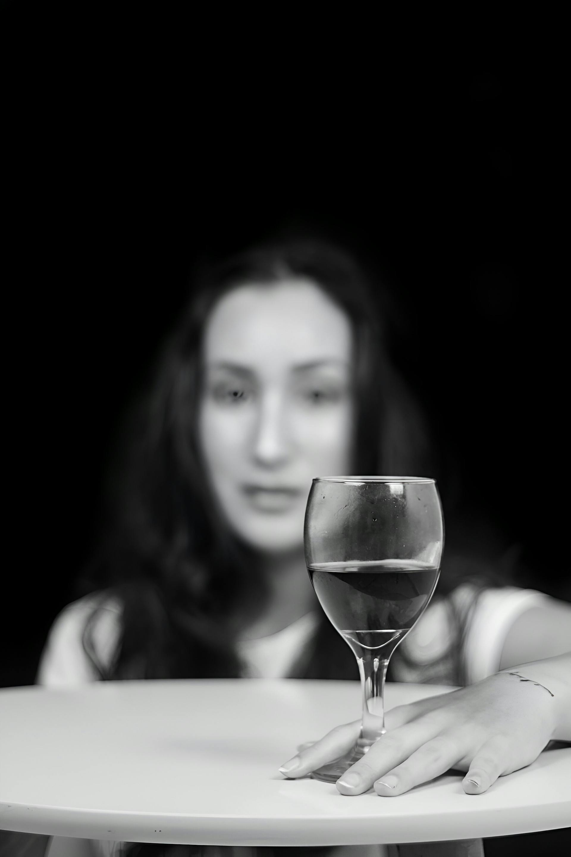 Nuances de gris d'une femme assise à une table avec un verre de vin | Source : Pexels