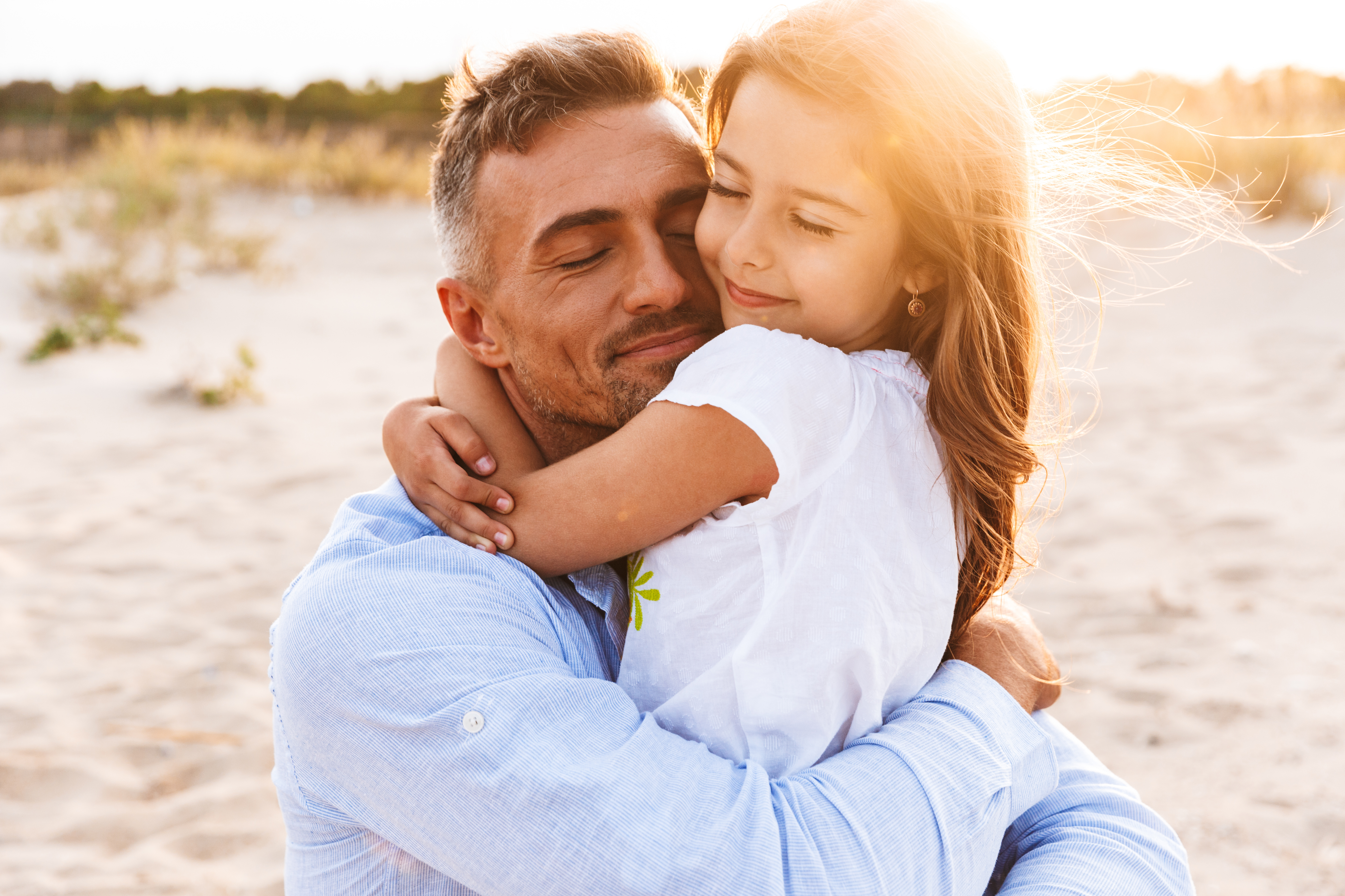 Père heureux serrant sa petite fille dans ses bras sur la plage | Source : Shutterstock