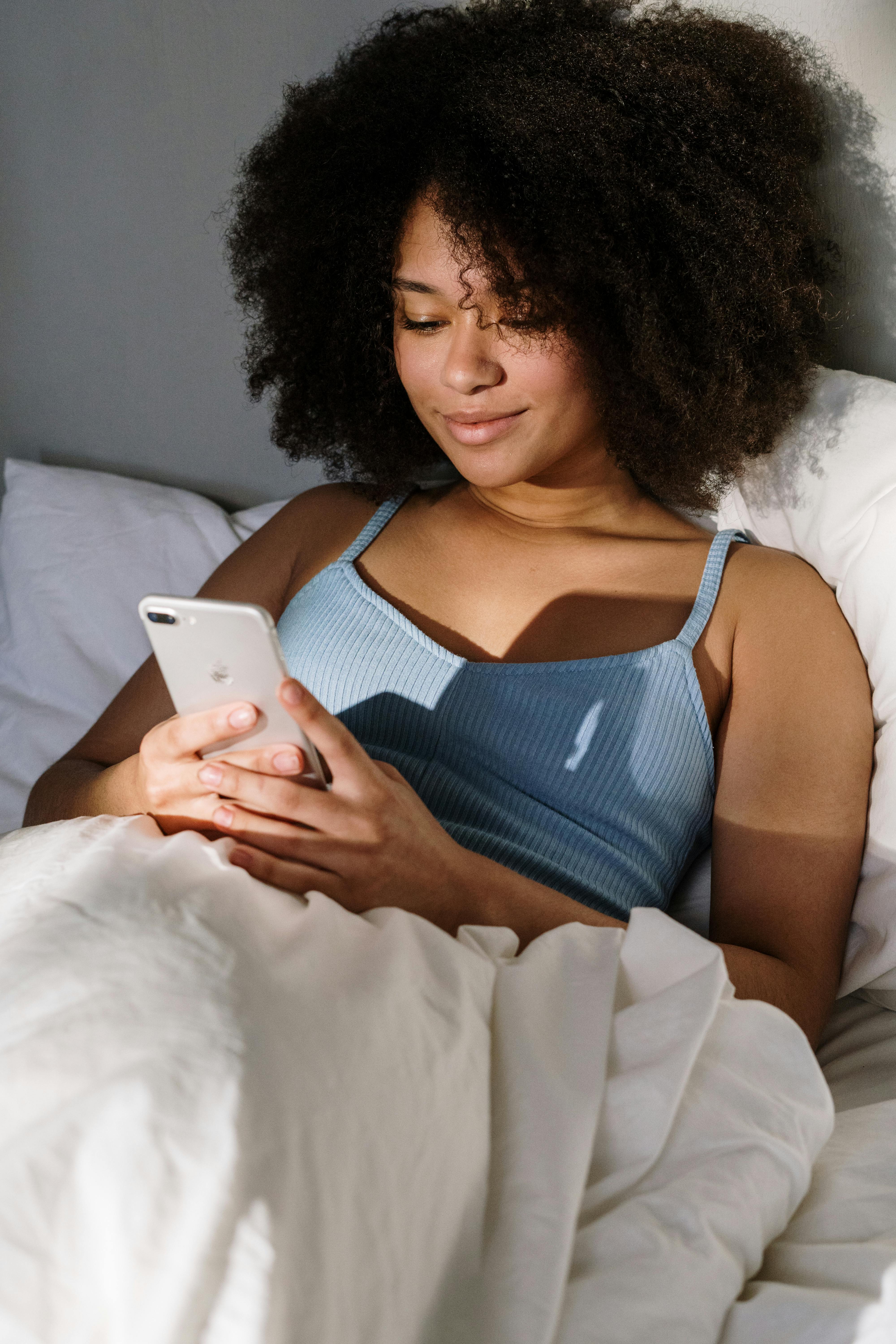 Une femme qui sourit en regardant son téléphone au lit | Source : Pexels