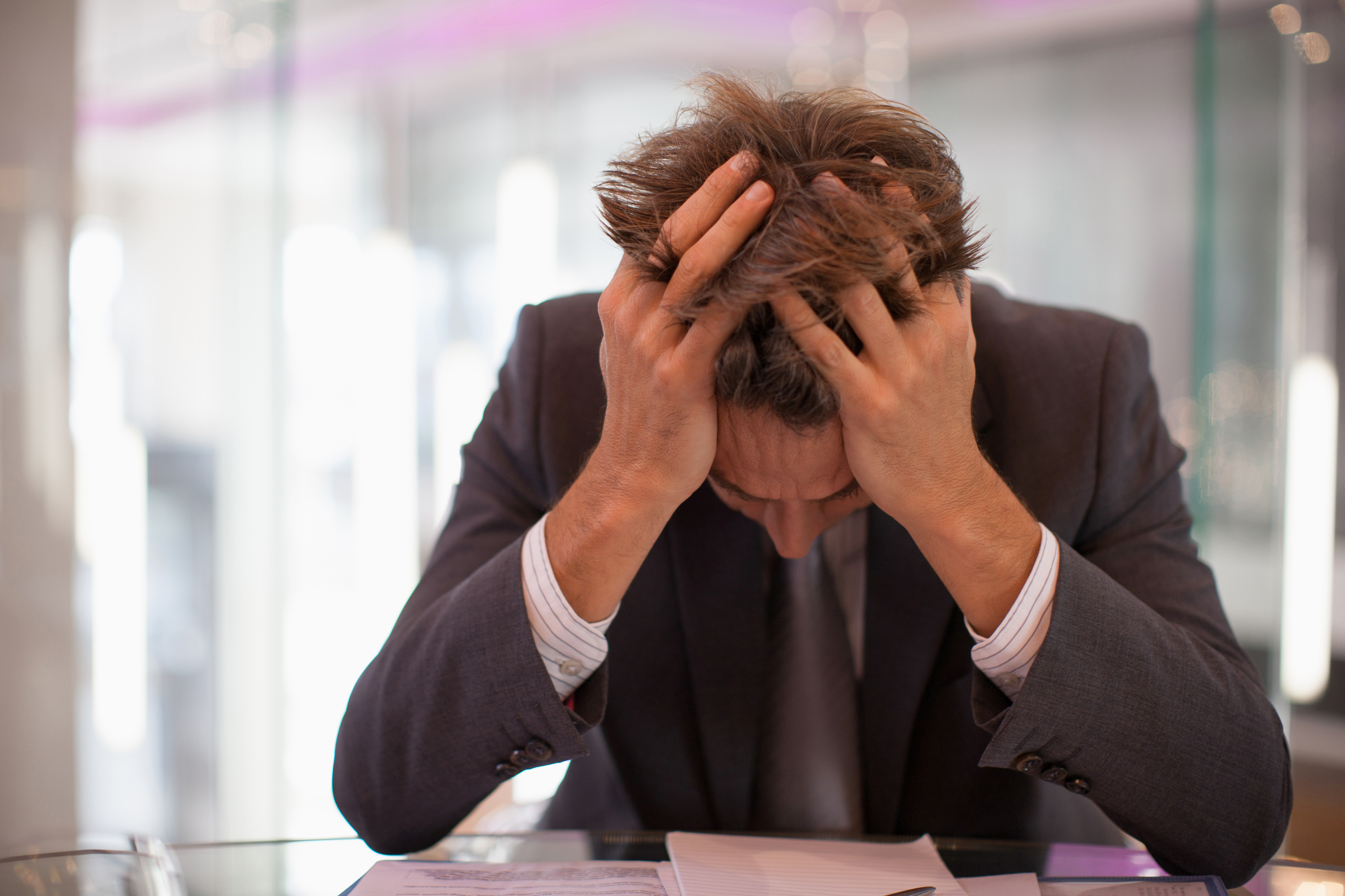 Homme d'affaires frustré assis à son bureau, la tête dans les mains | Source : Getty Images