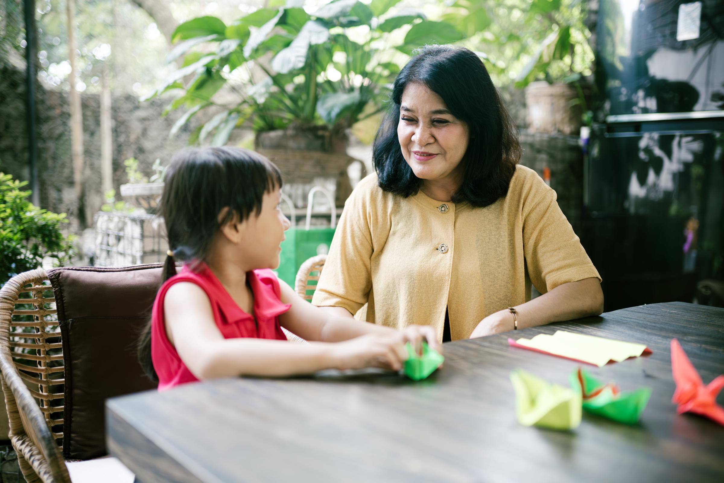 Une grand-mère sourit à sa petite-fille après avoir fait des origamis ensemble à la maison. | Source : Getty Images