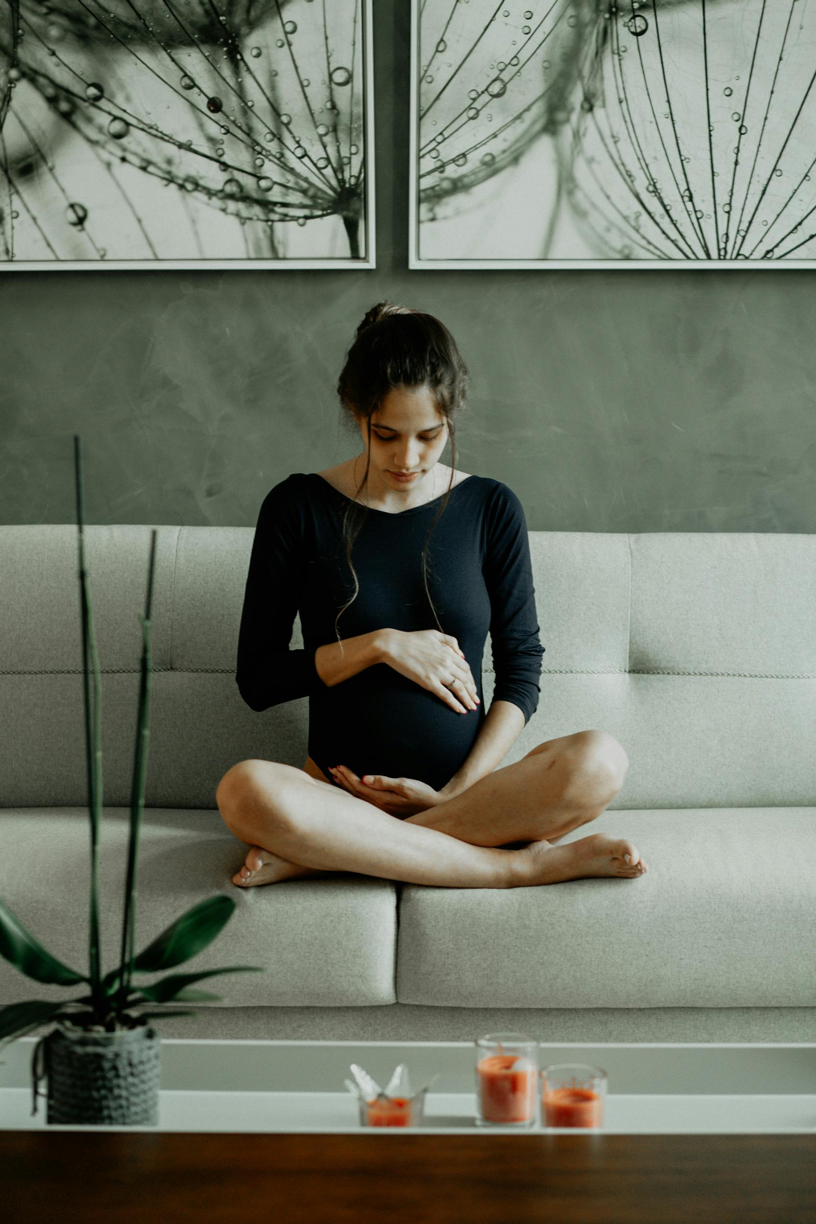 Une femme enceinte assise sur le canapé tout en se touchant le ventre | Source : Pexels