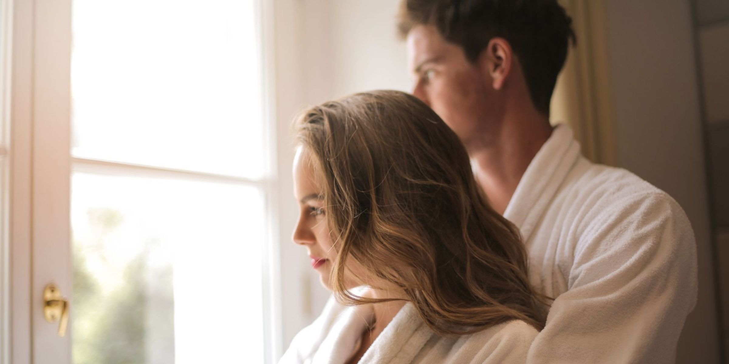 Un couple en peignoir blanc, debout côte à côte près d'une fenêtre baignée de soleil | Source : Pexels