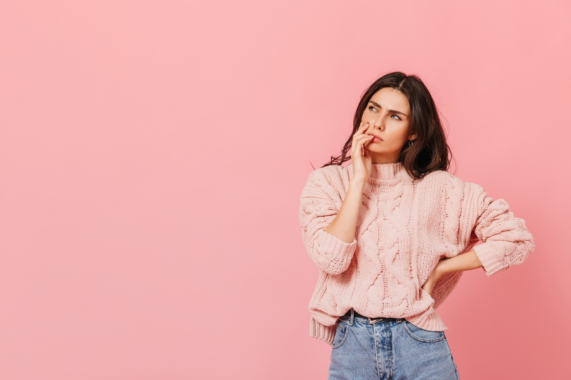 Une femme avec un pull rose, en train de réfléchir | Source : Freepik