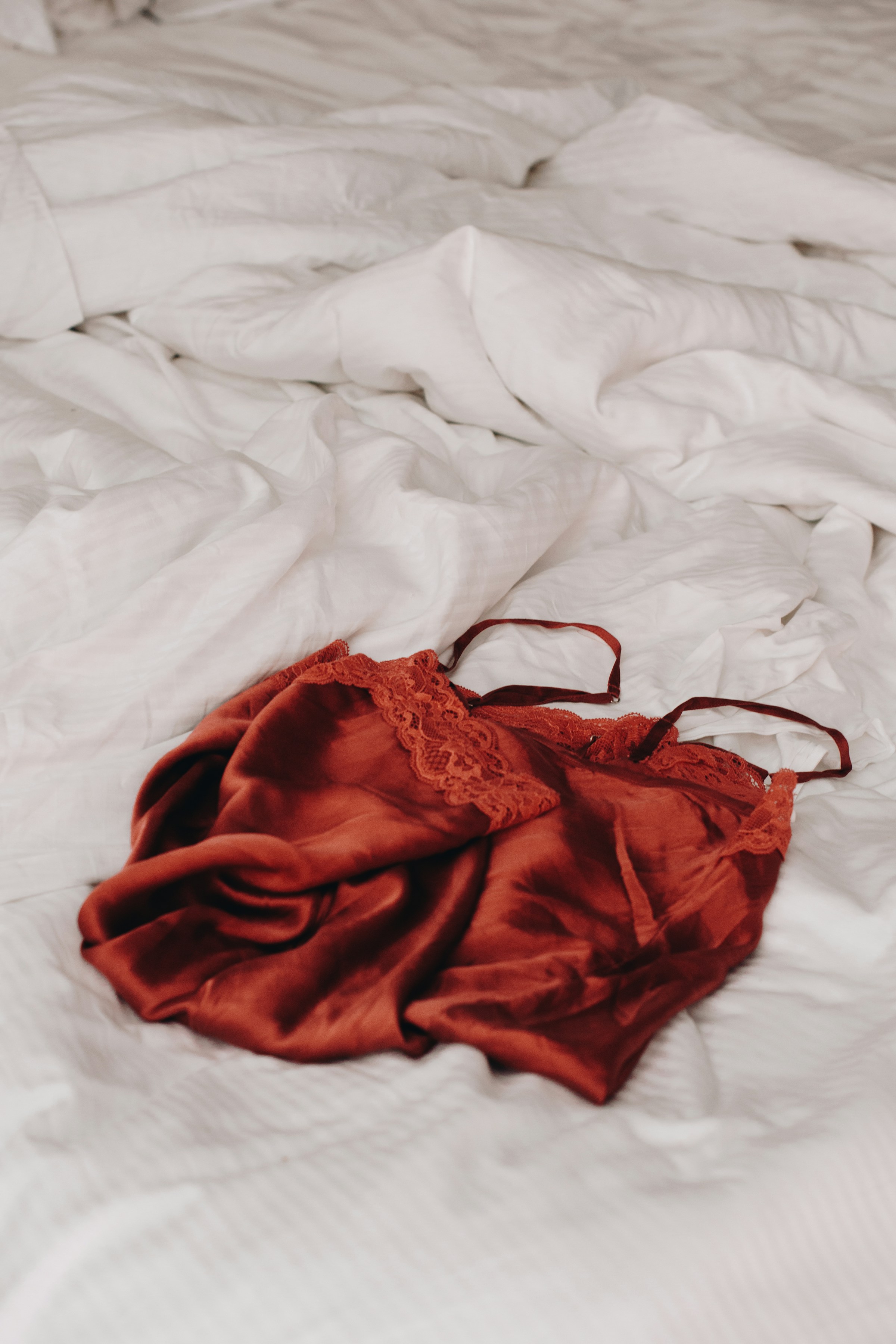 Lingerie rouge à lacets posée sur des draps blancs en lin | Source : Unsplash