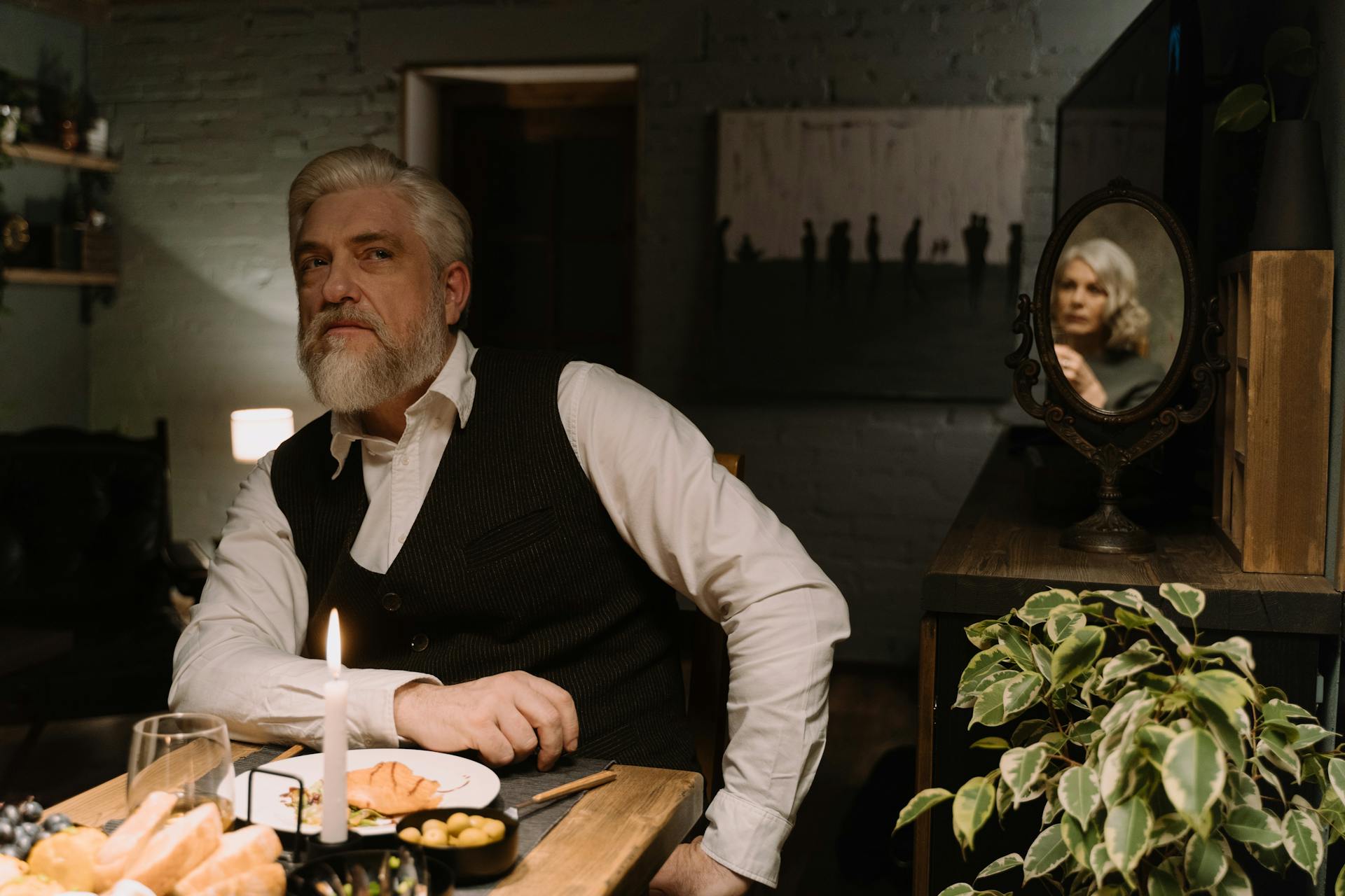 Un homme âgé assis dans une salle à manger tandis qu'un miroir projette le reflet de sa partenaire sur la table derrière | Source : Pexels