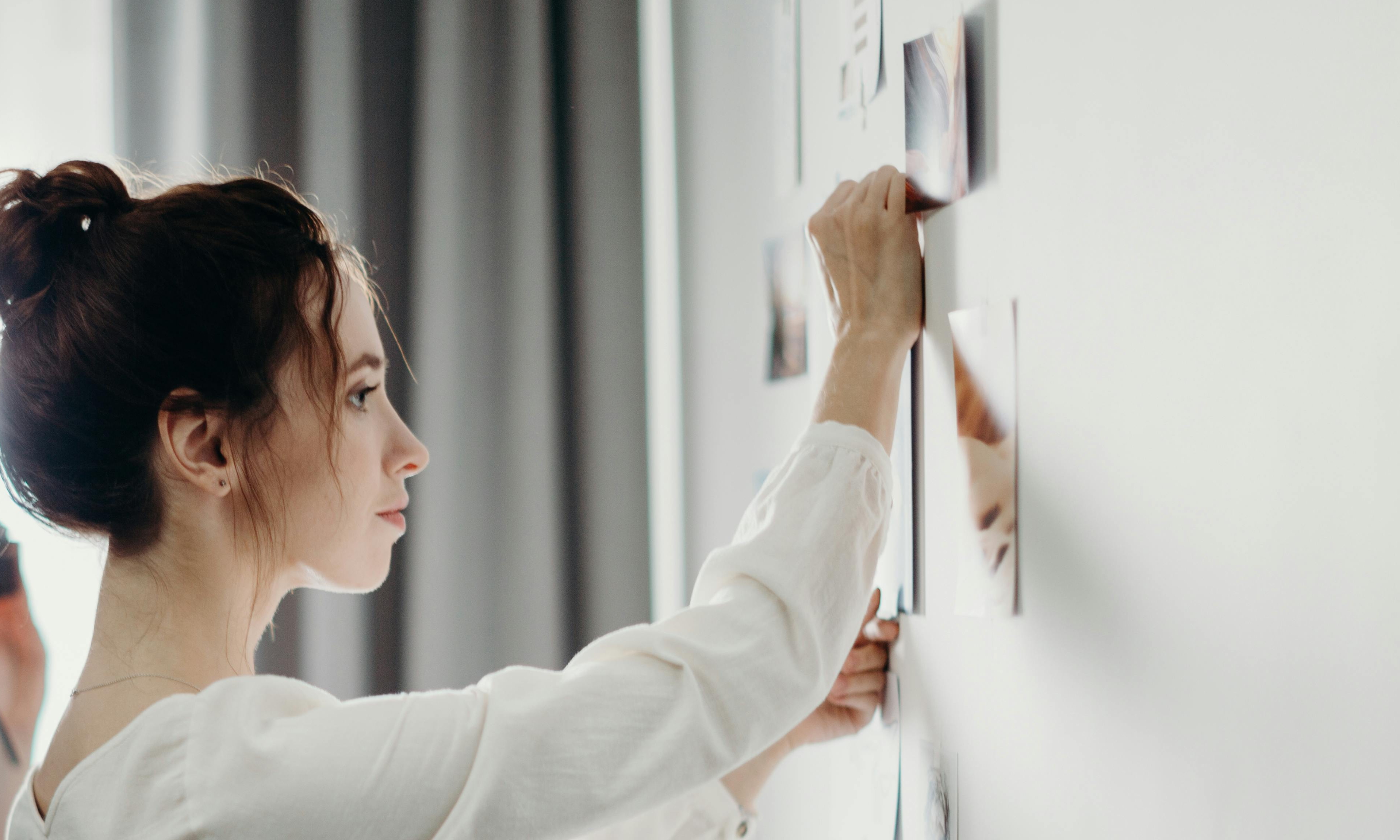 Une jeune femme colle une photographie sur un mur | Source : Pexels