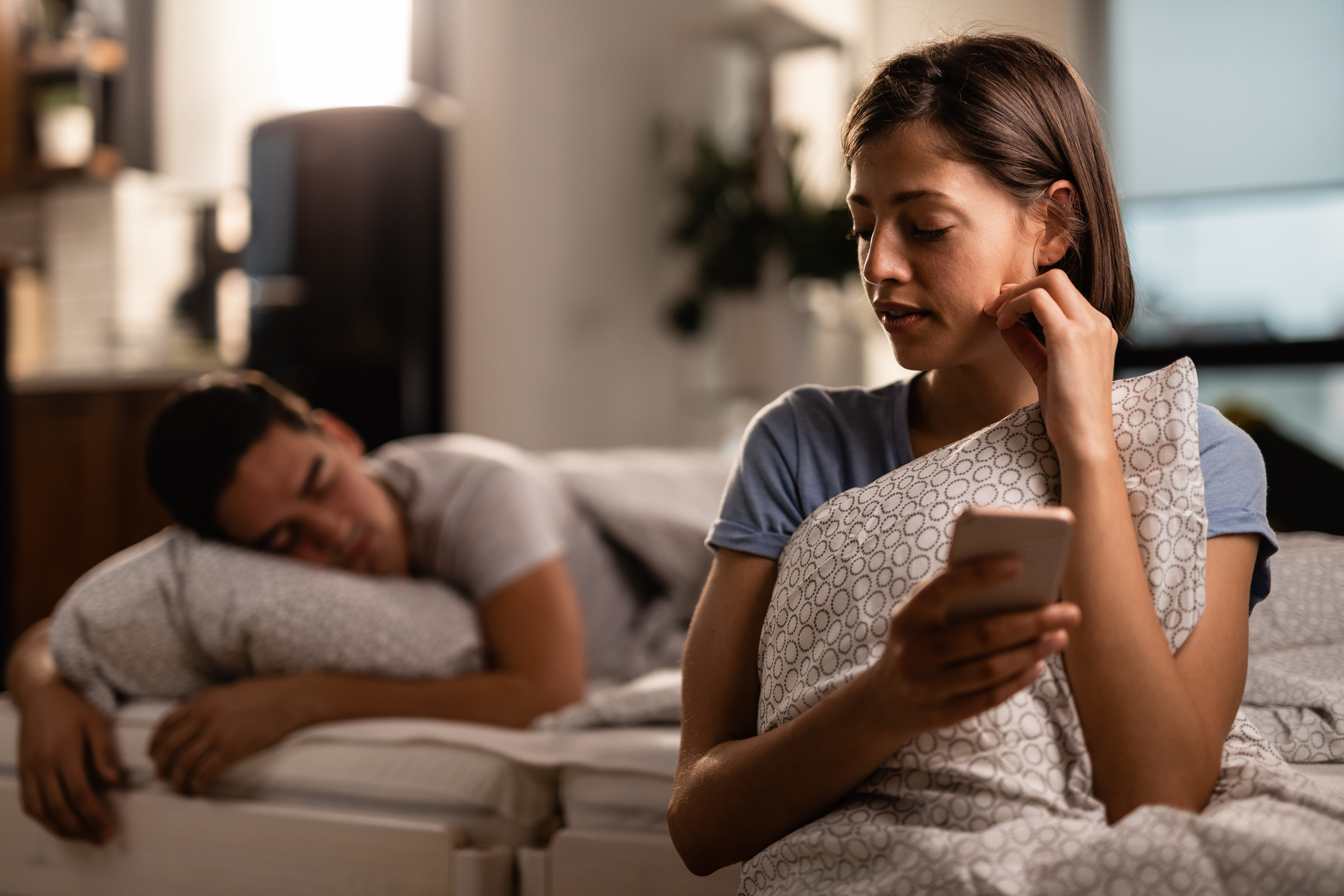 Une femme consulte secrètement son téléphone pendant que son partenaire fait la sieste | Source : Shutterstock