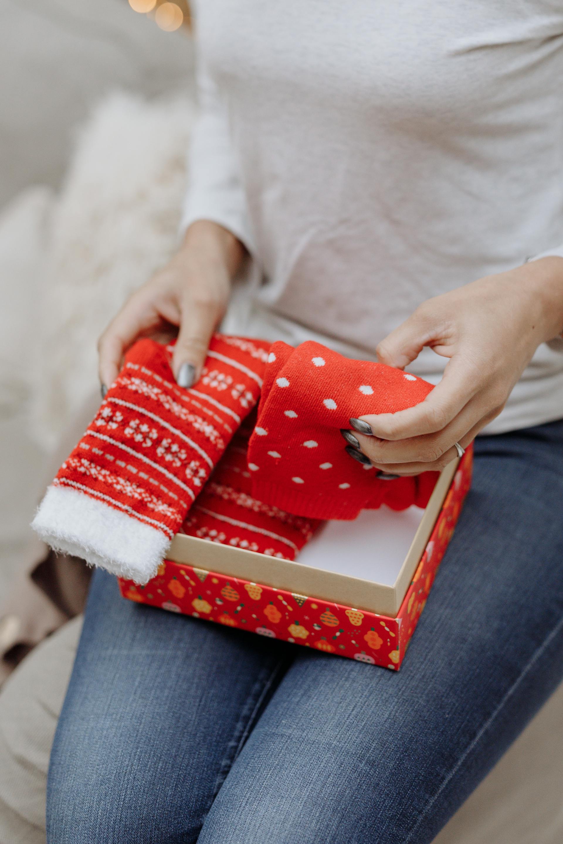 Gros plan sur une femme tenant des chaussettes de Noël allongées dans un paquet cadeau rouge | Source : Pexels